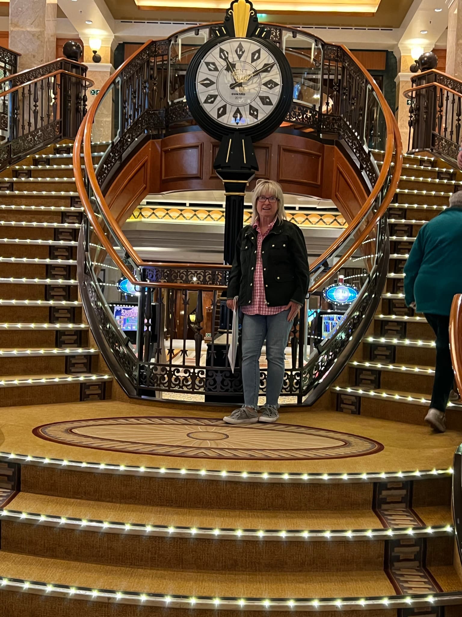 Travel advisor posing inside of the ship before an old-fashioned style clock and curved staircases.