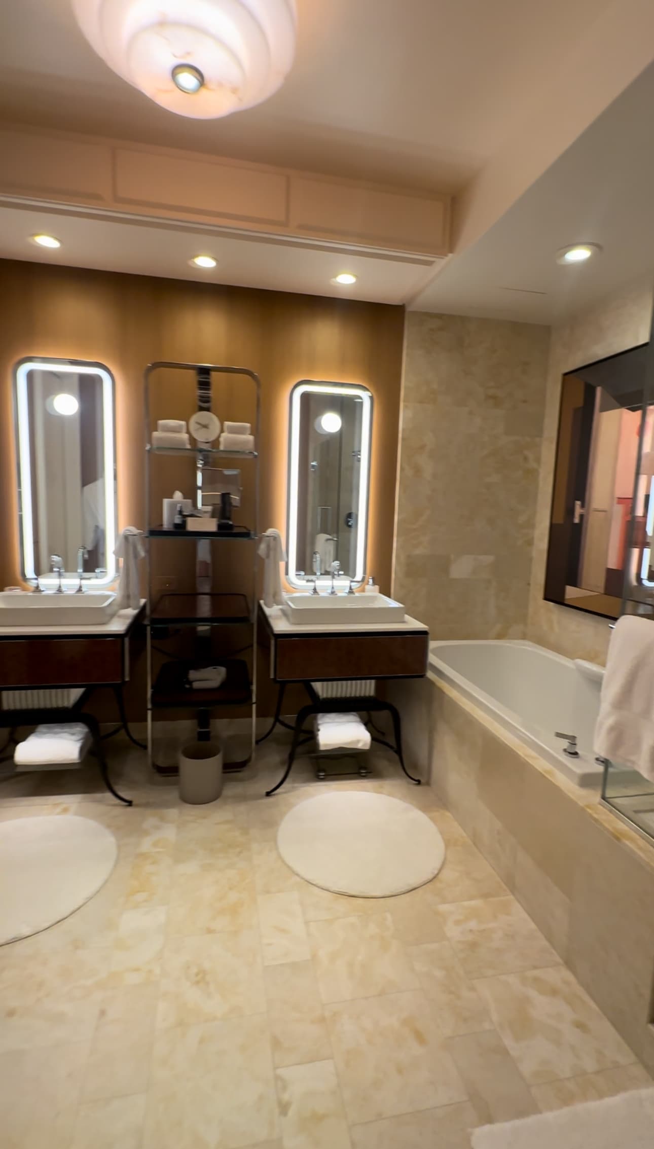 Inside the hotel room's bathroom with double sinks, a luxurious tub and mirrors with lights around them.