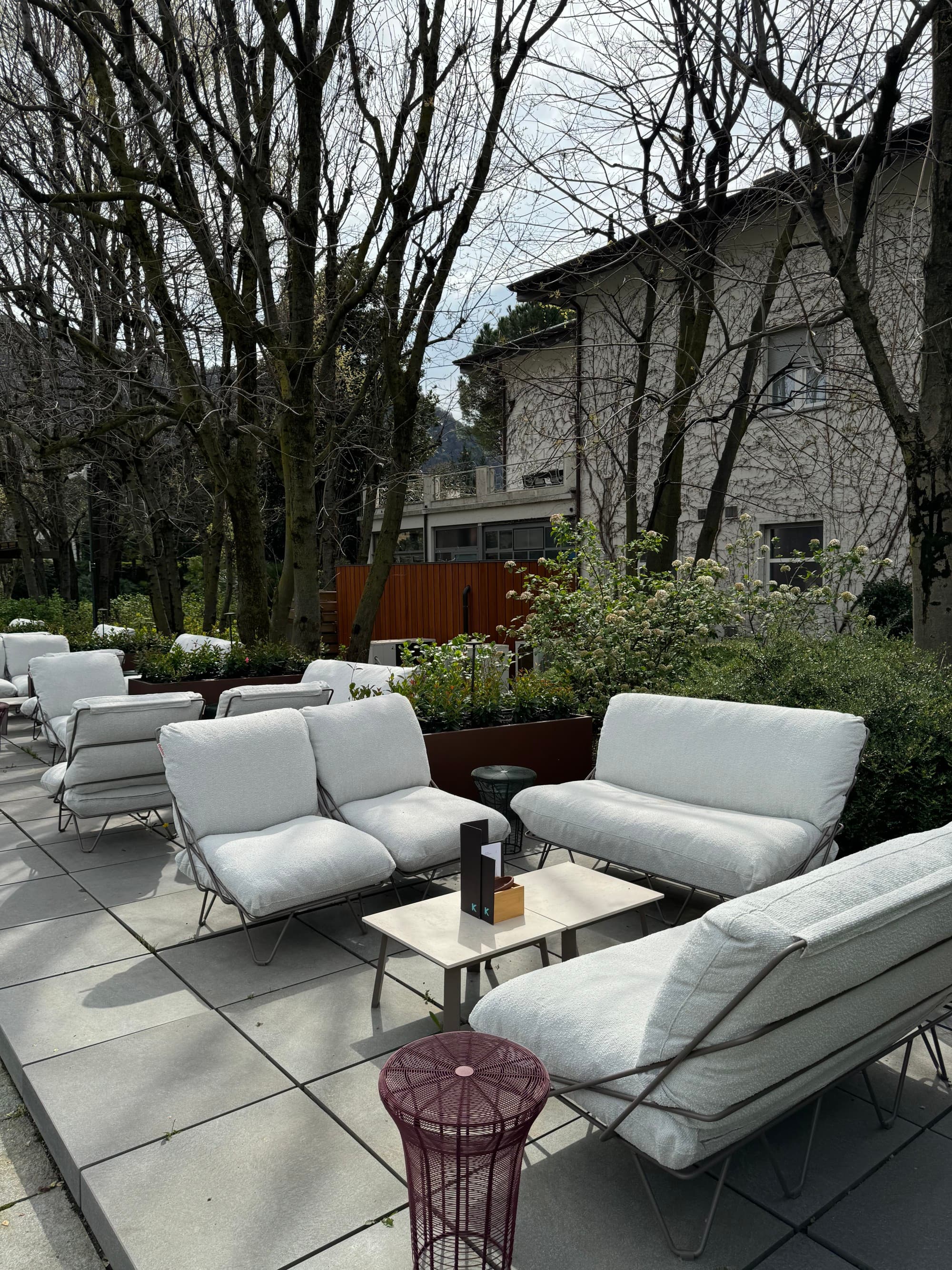 An outdoor lounge area with white, cushioned chairs and trees surrounding it.