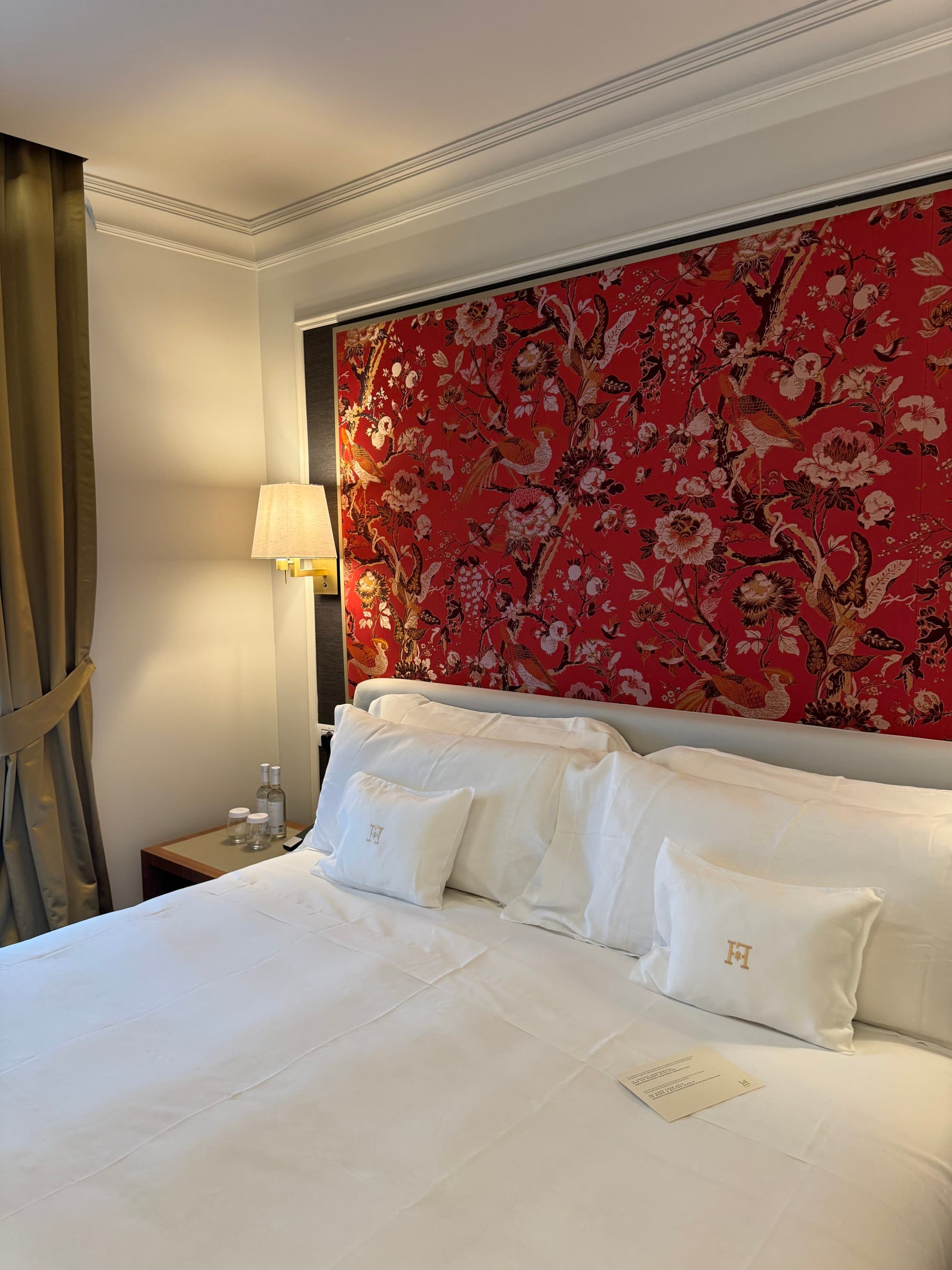 A bedroom with a white linen bed and a red floral headboard behind it.