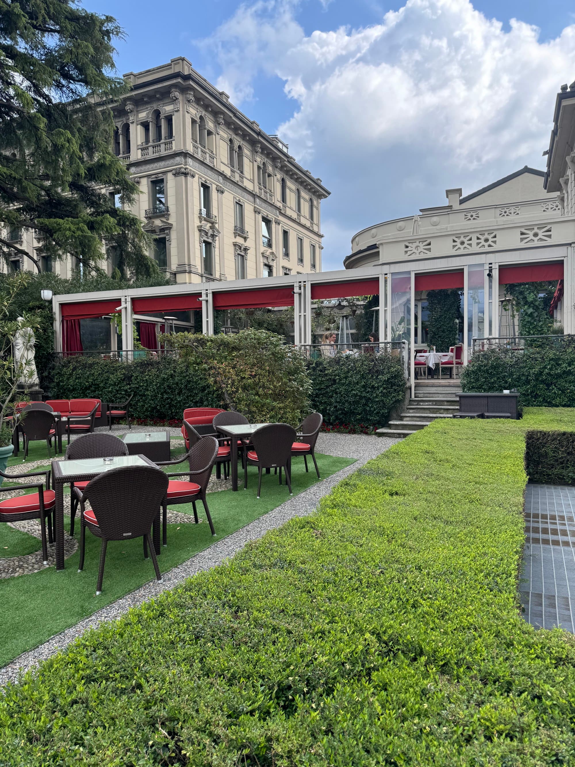 An outdoor dining area behind the hotel in the middle of a green garden.