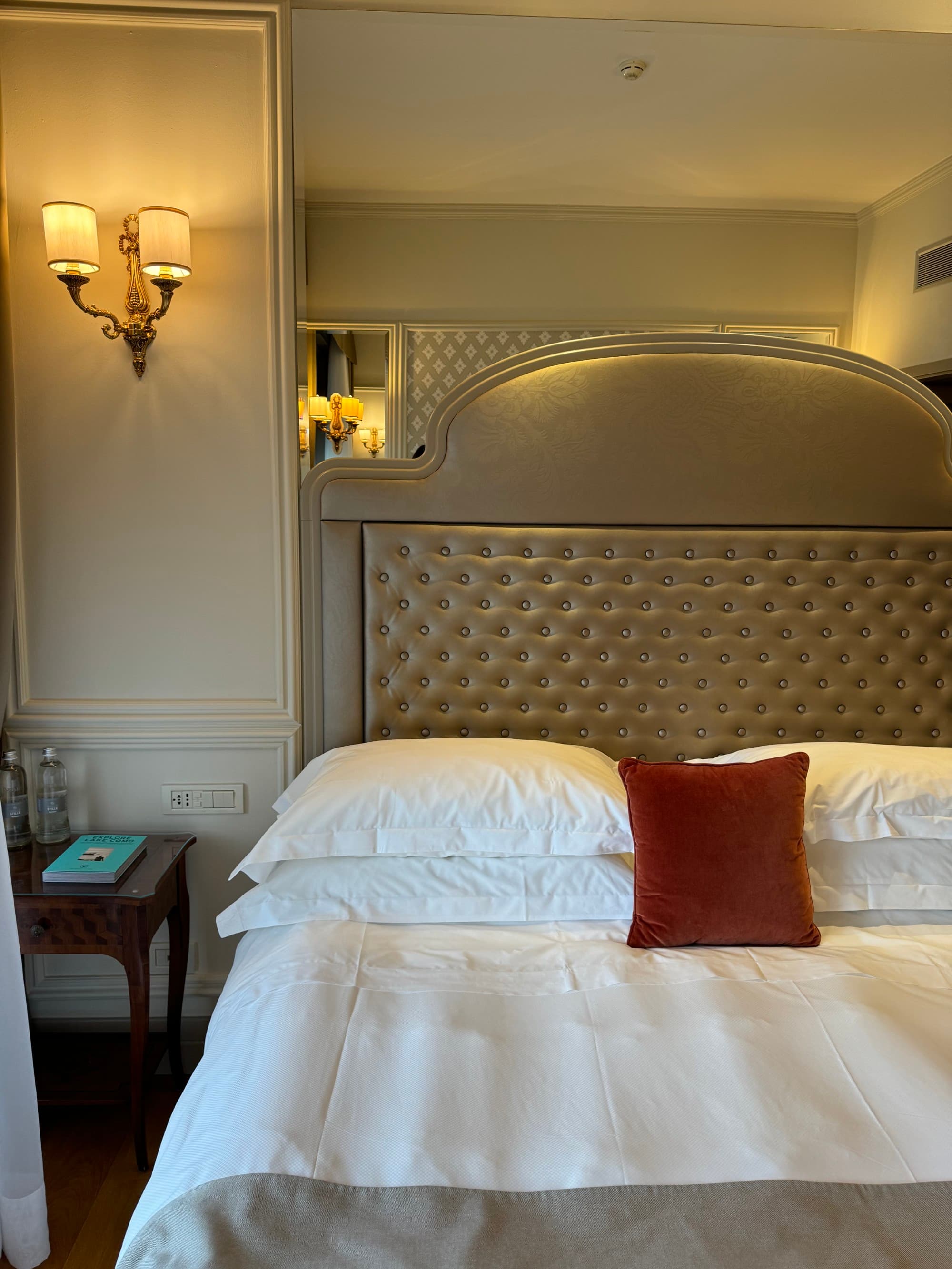 A photo of a hotel room bed with white linens and a leather gray headboard.