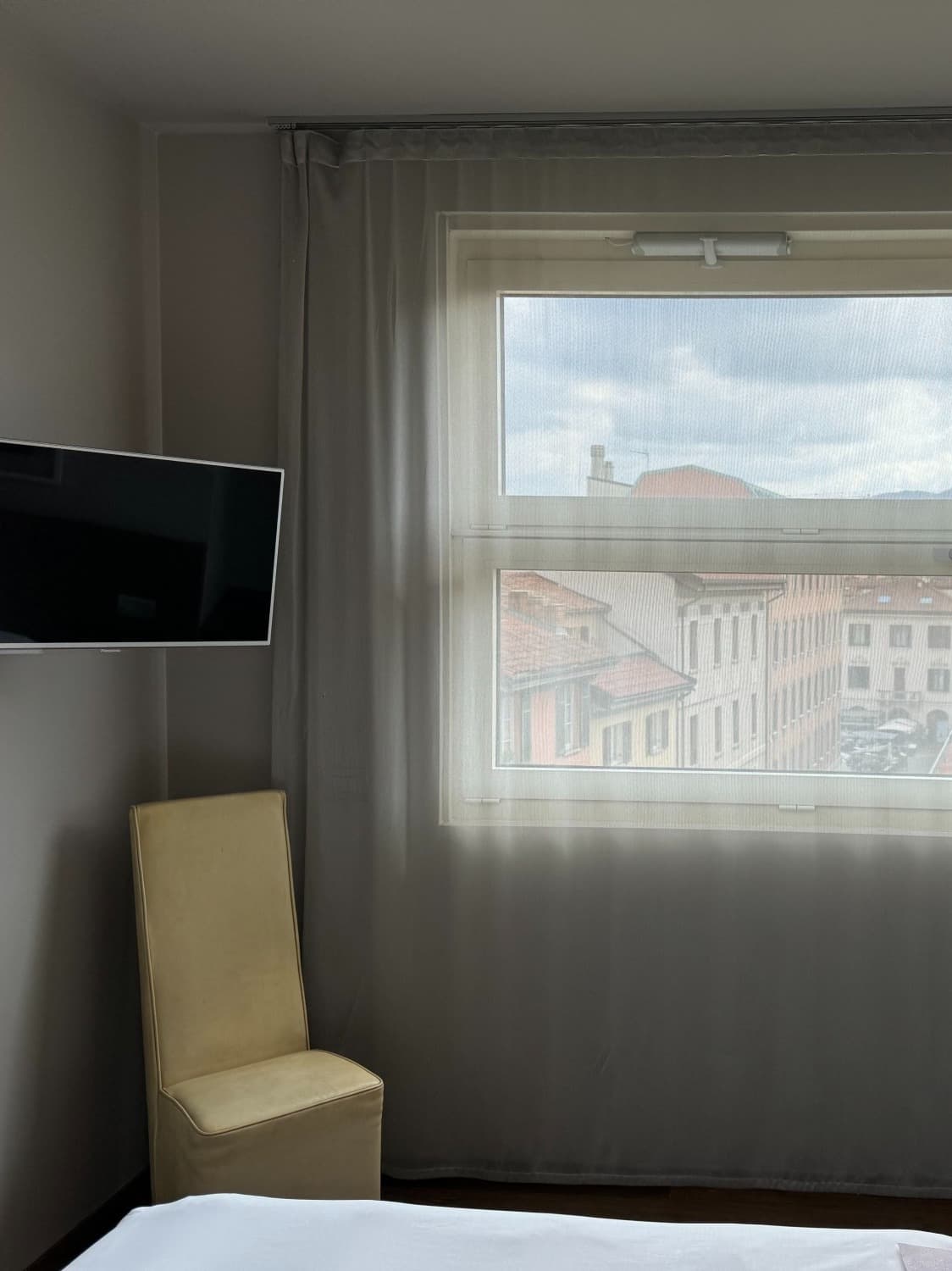 A photo inside a hotel room of a window with sheer curtains drawn and a silhouette of an Italian city behind them.