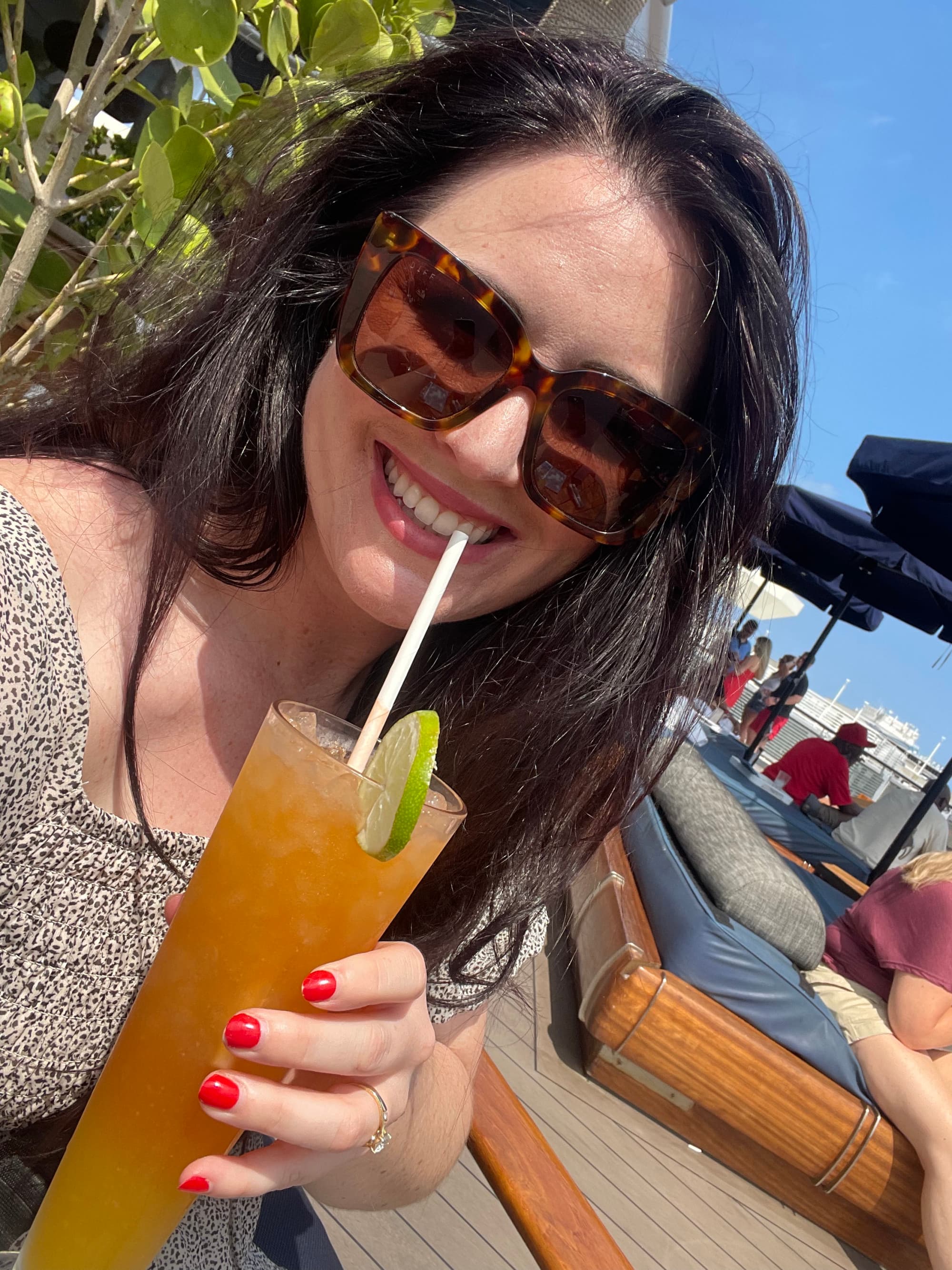 Travel advisor Jacqueline posing with a drink in a long glass with a slice of lime and a straw with sun loungers behind.