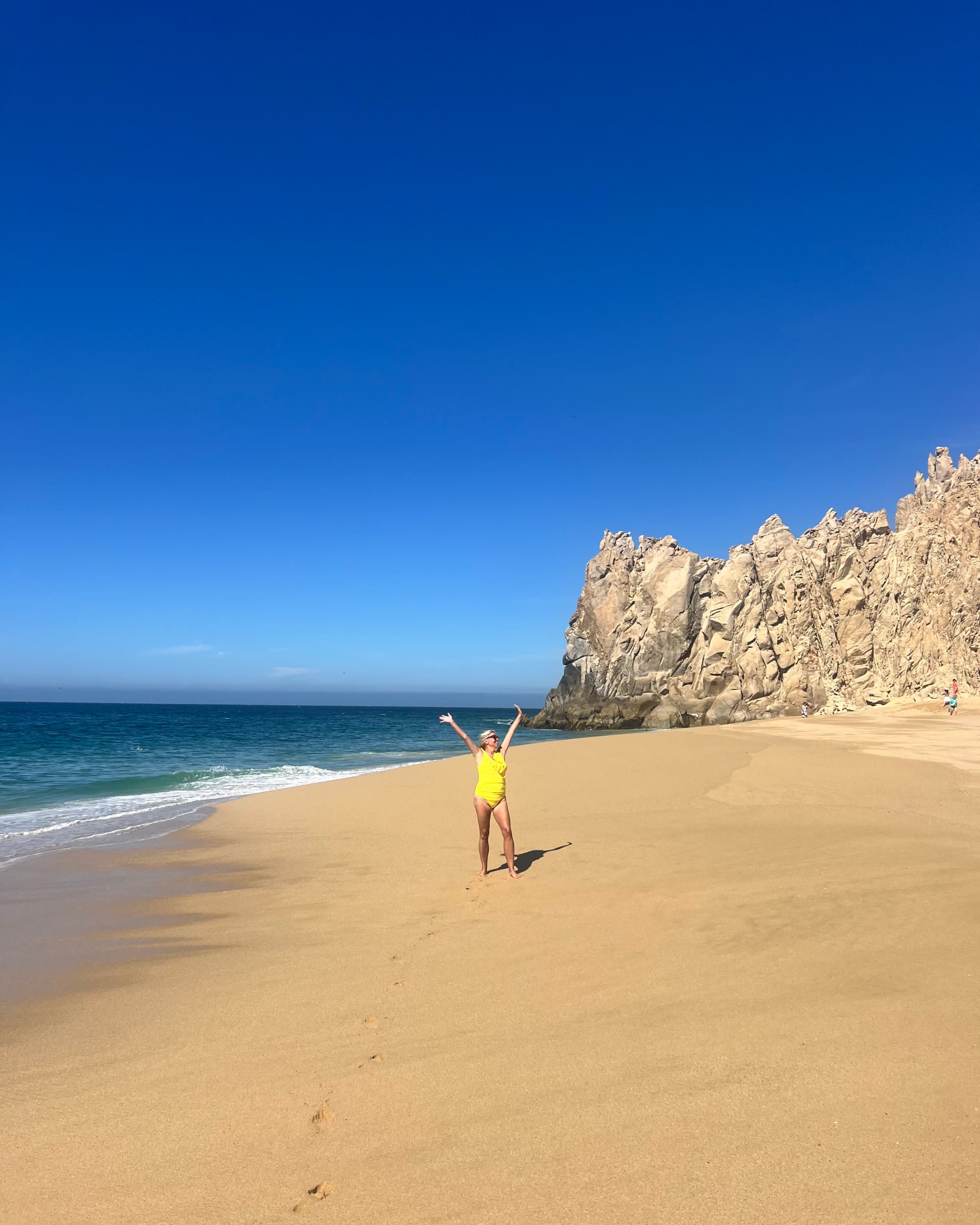 Joelle in a yellow swimsuit posing on Divorce Beach with rocks in the background.