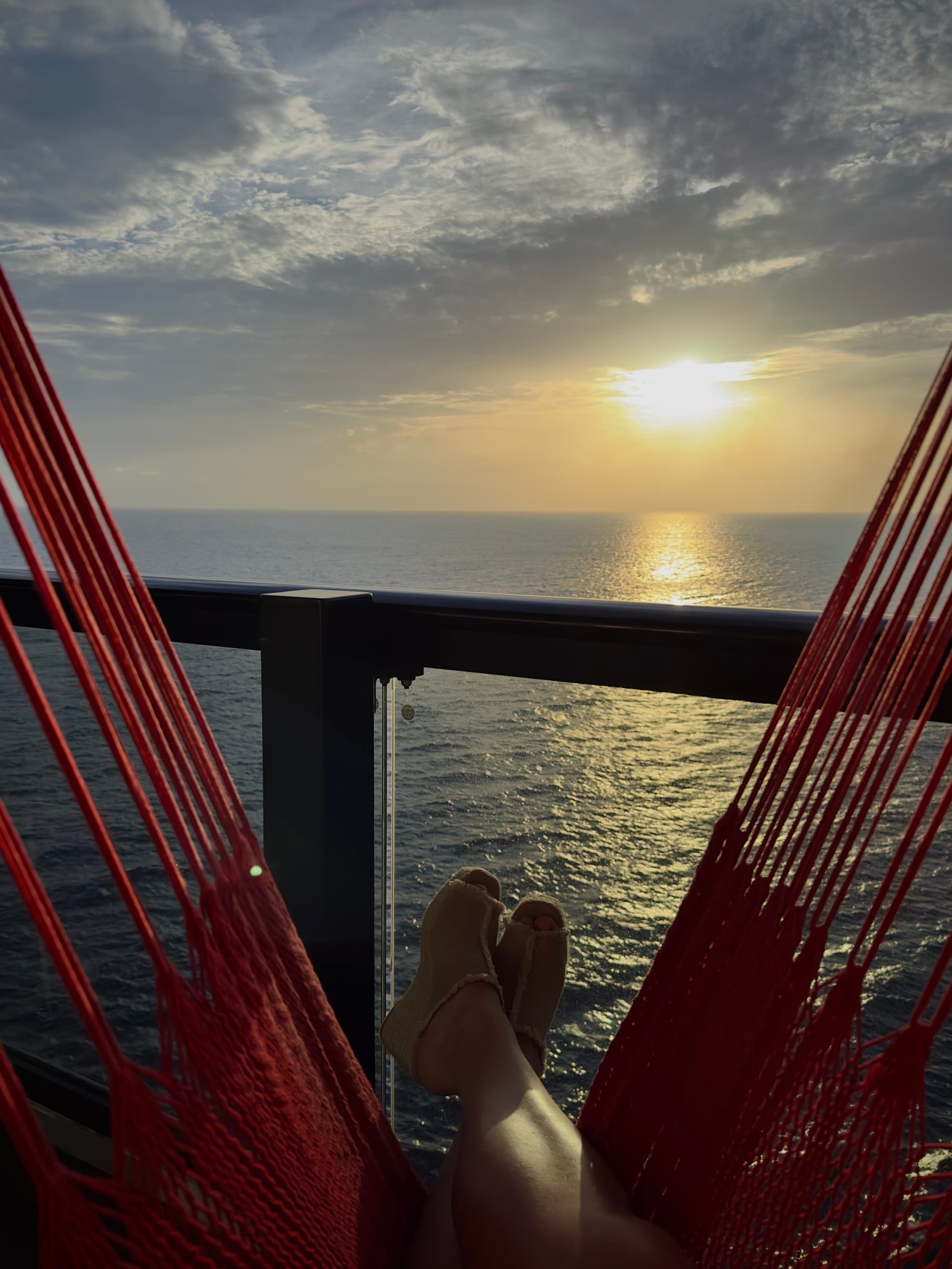 Sunset over the ocean, as seen from a red hammock on Virgin Voyages Valiant Lady - Kelsey Parry