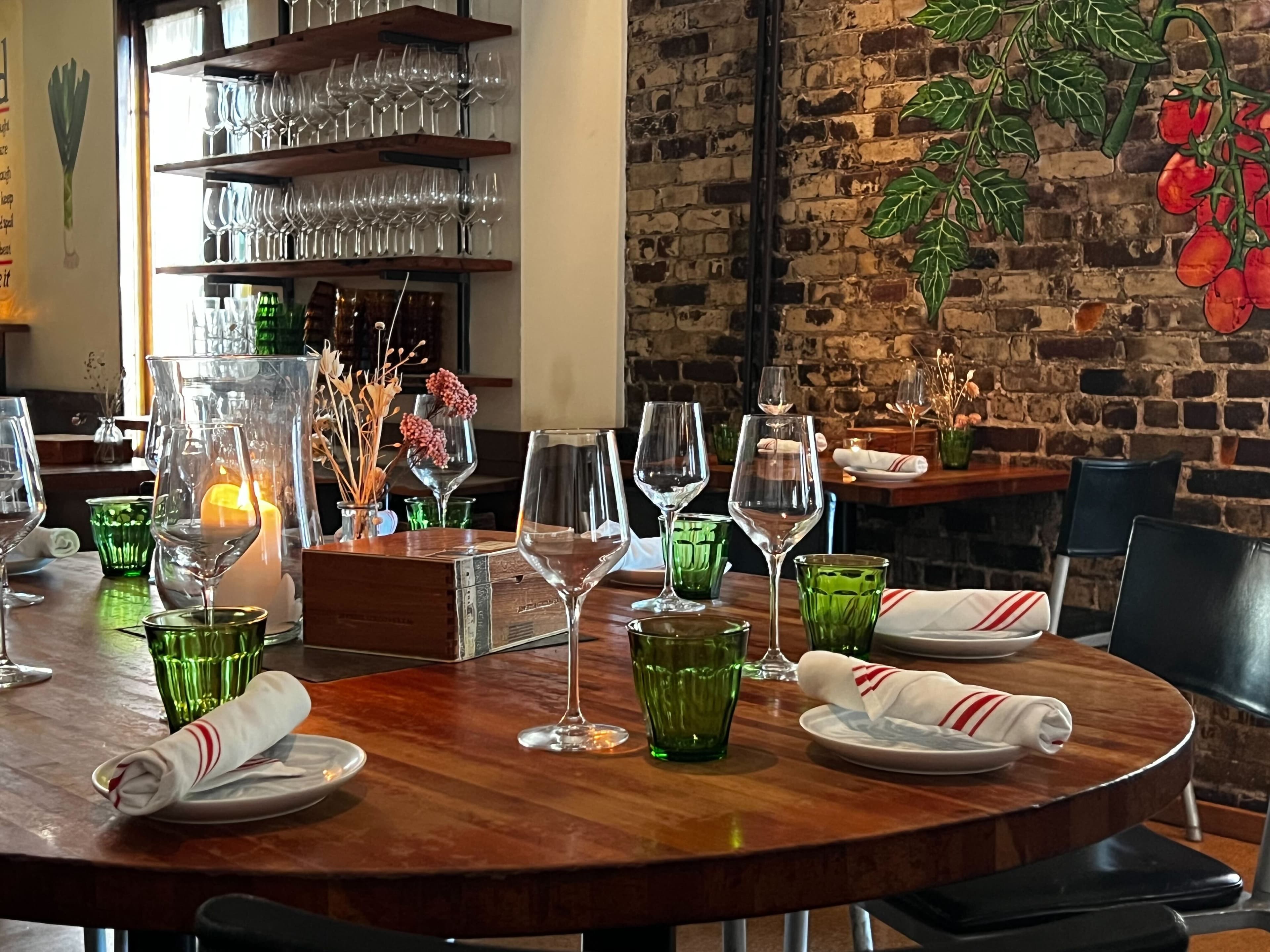 a round set table with green water glasses and wine glasses in front of a brick wall