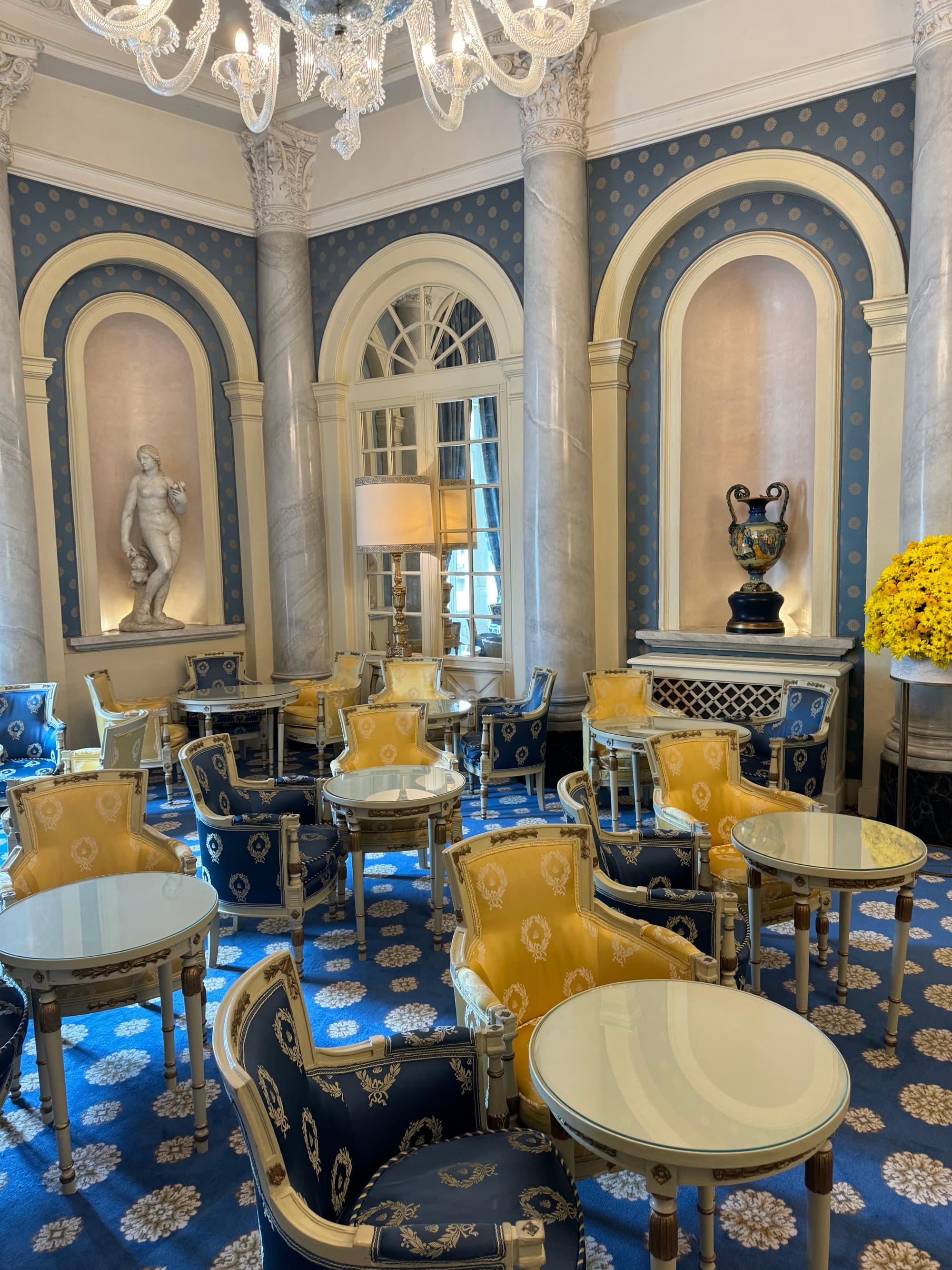 Hotel dining area consisting of marble tables and cozy armchairs scatter the well-lit arched room.