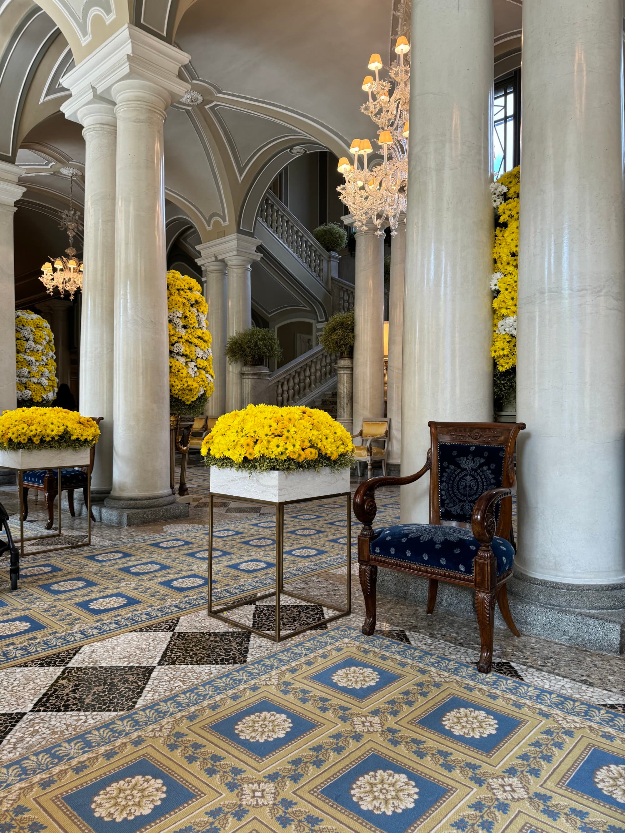 The hotel interior is decorated with tiled floors scattered with rich rugs, antique chairs and potted flora.