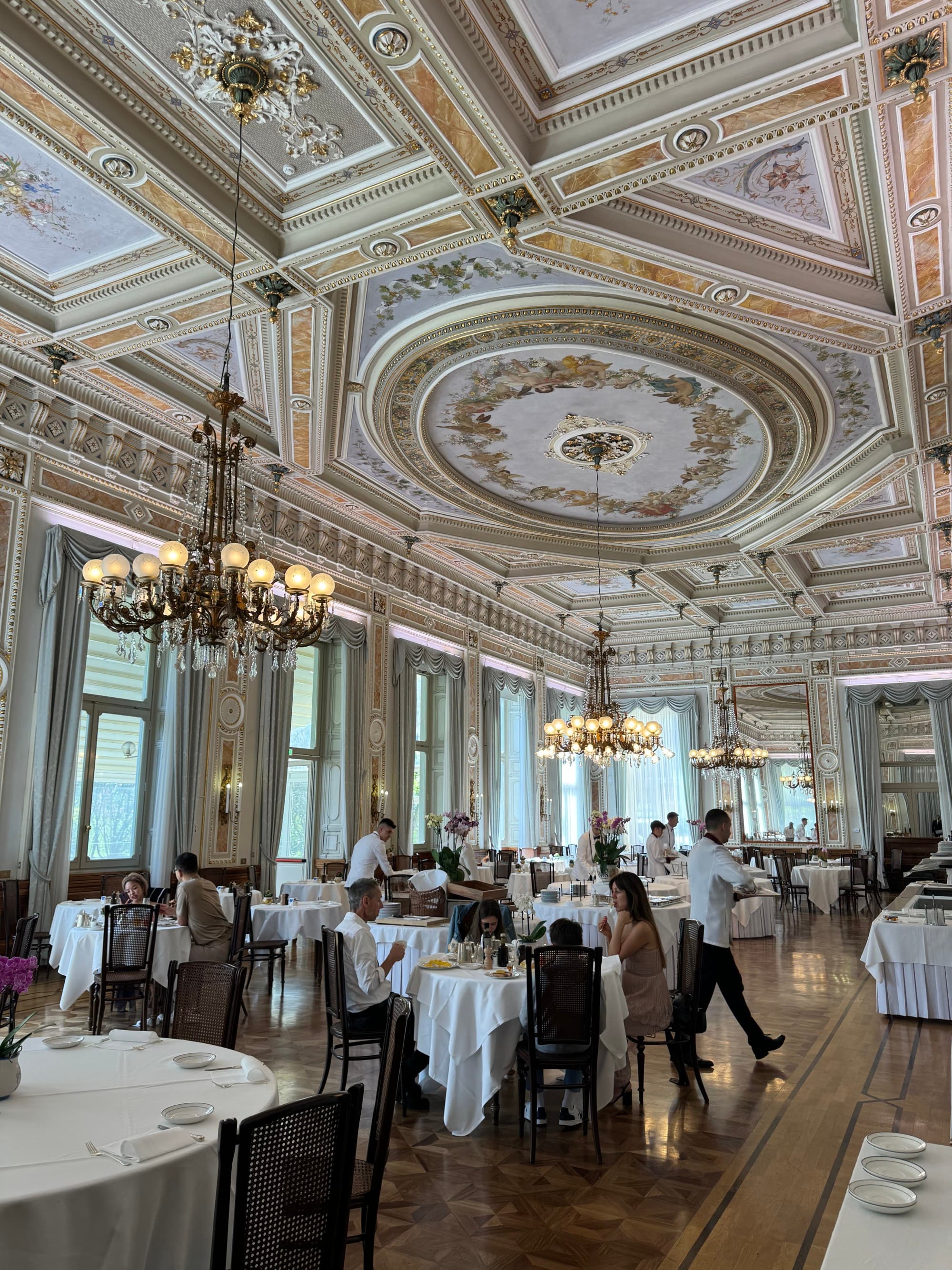 Inside dining area with high ceilings as waiters take orders amid busy tables.