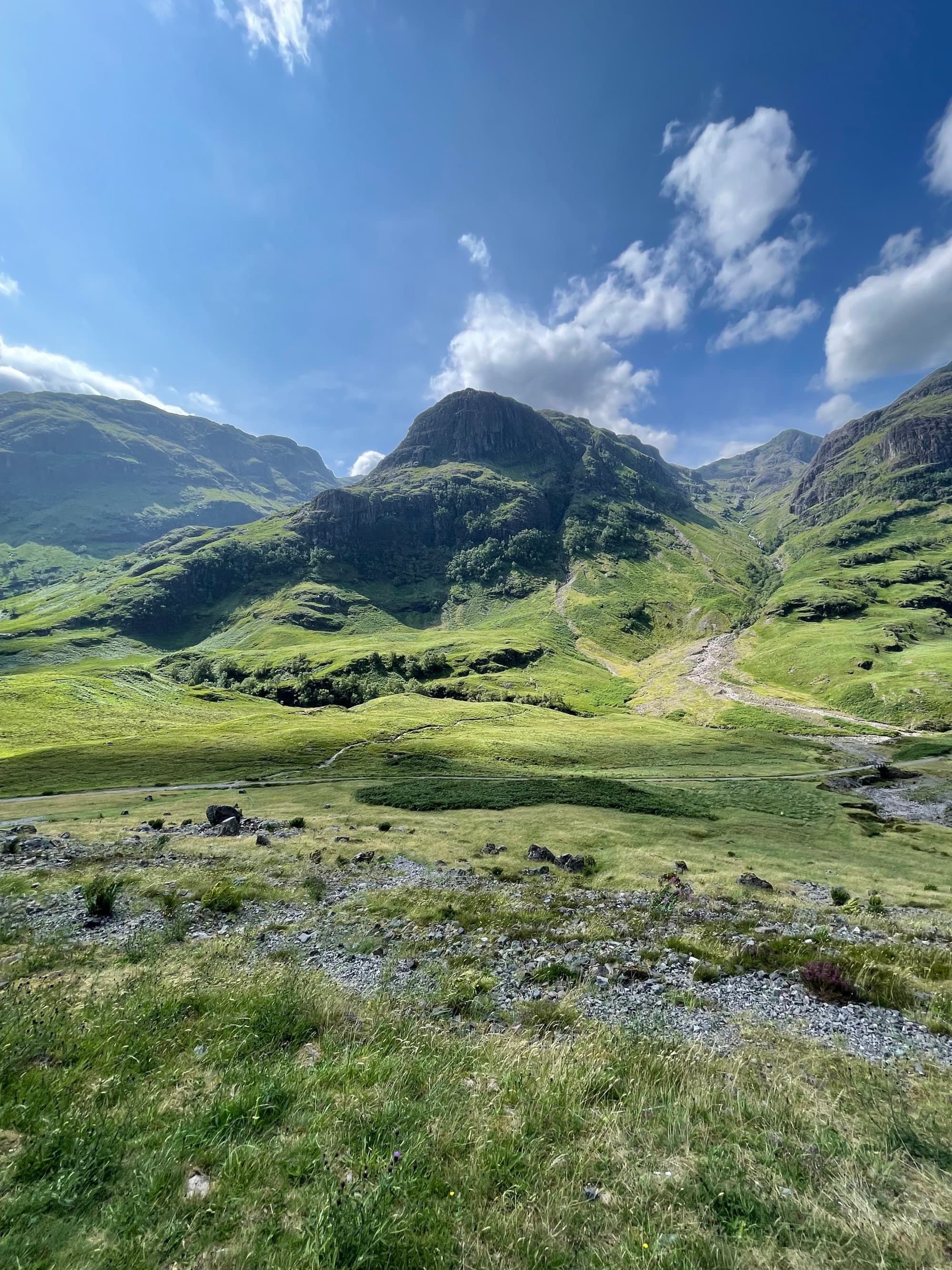 A view of a green grassy hillside and mountains in Edinburgh during the day.