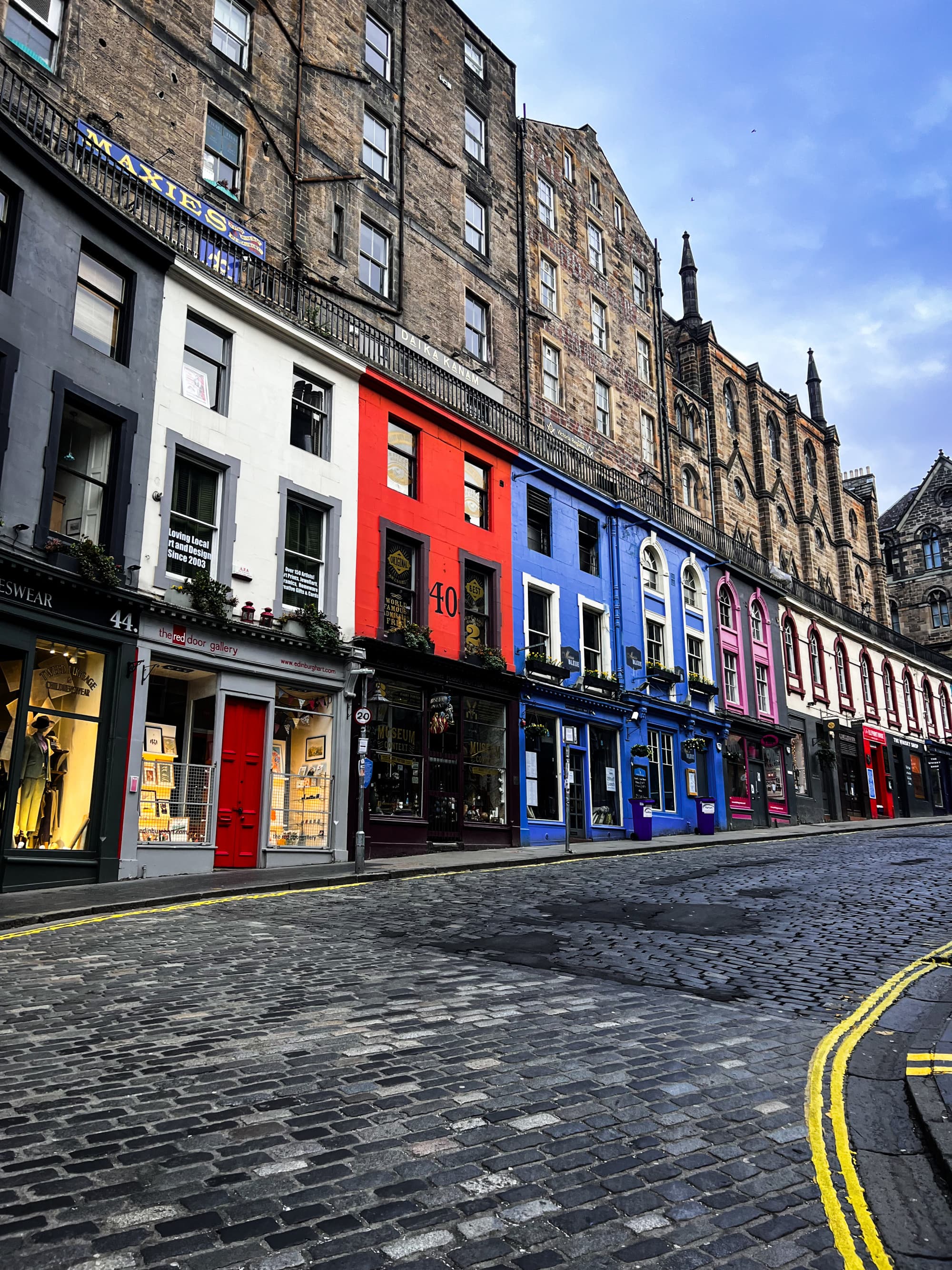 Princess Street in Edinburgh features brightly colored buildings lining a cobbled street on a sun-lit day.