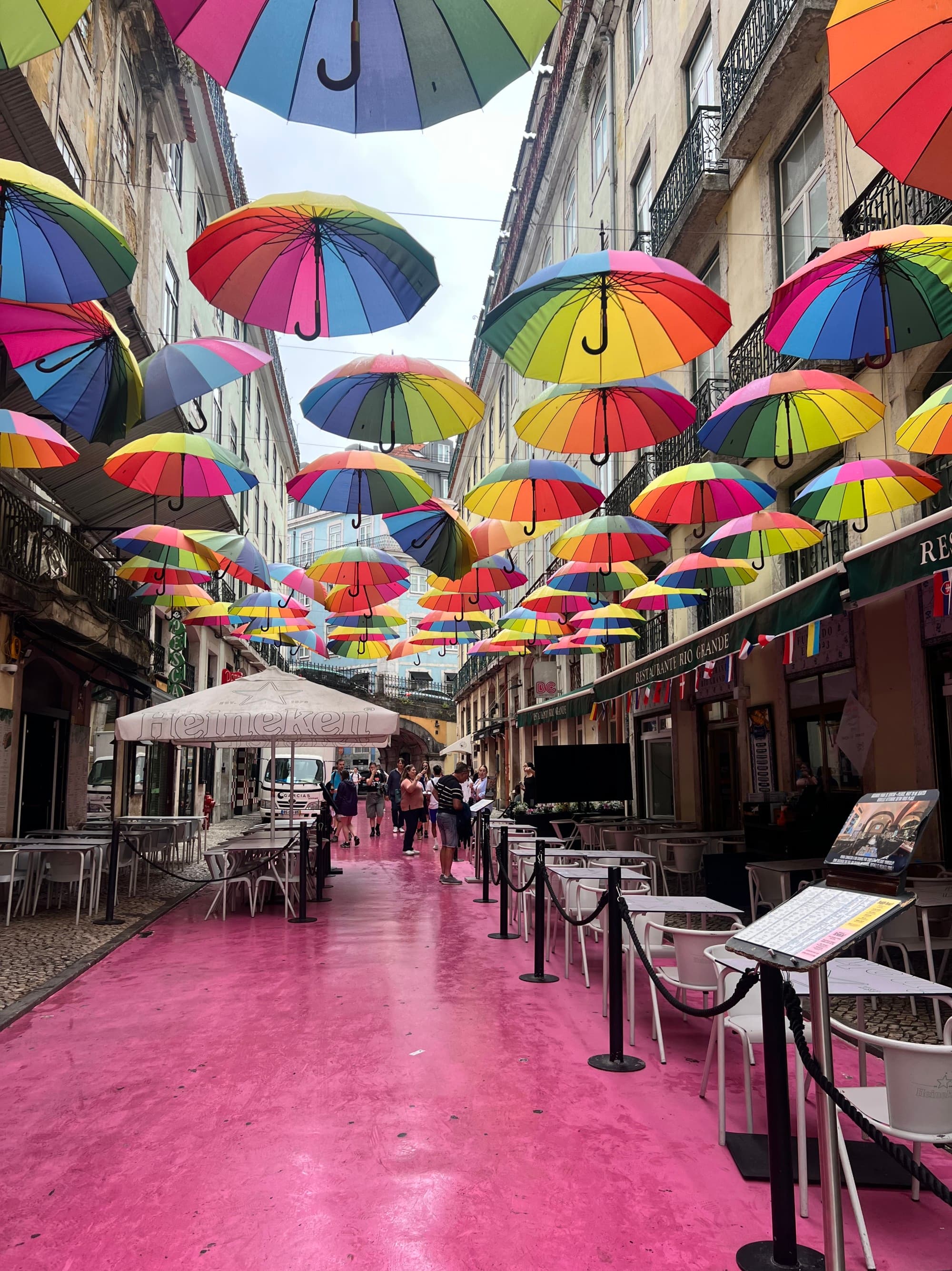 Pink street with rainbow umbrellas hung above.