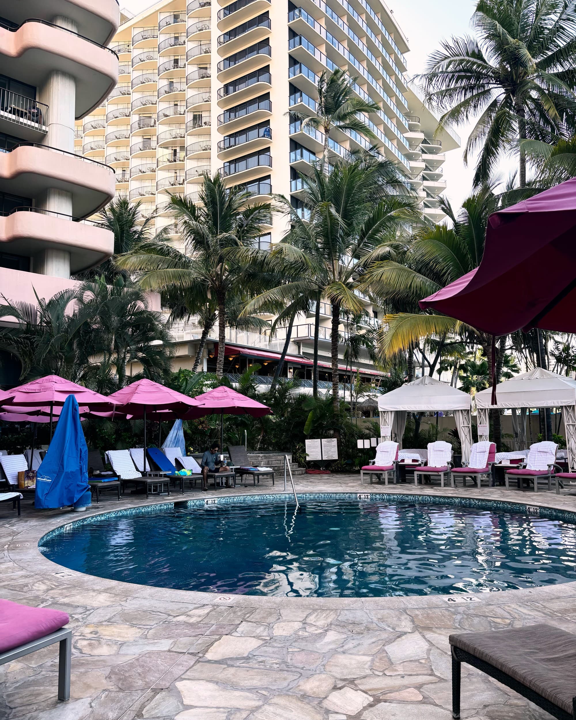 Pool with flagstones around it and pink shade umbrellas.