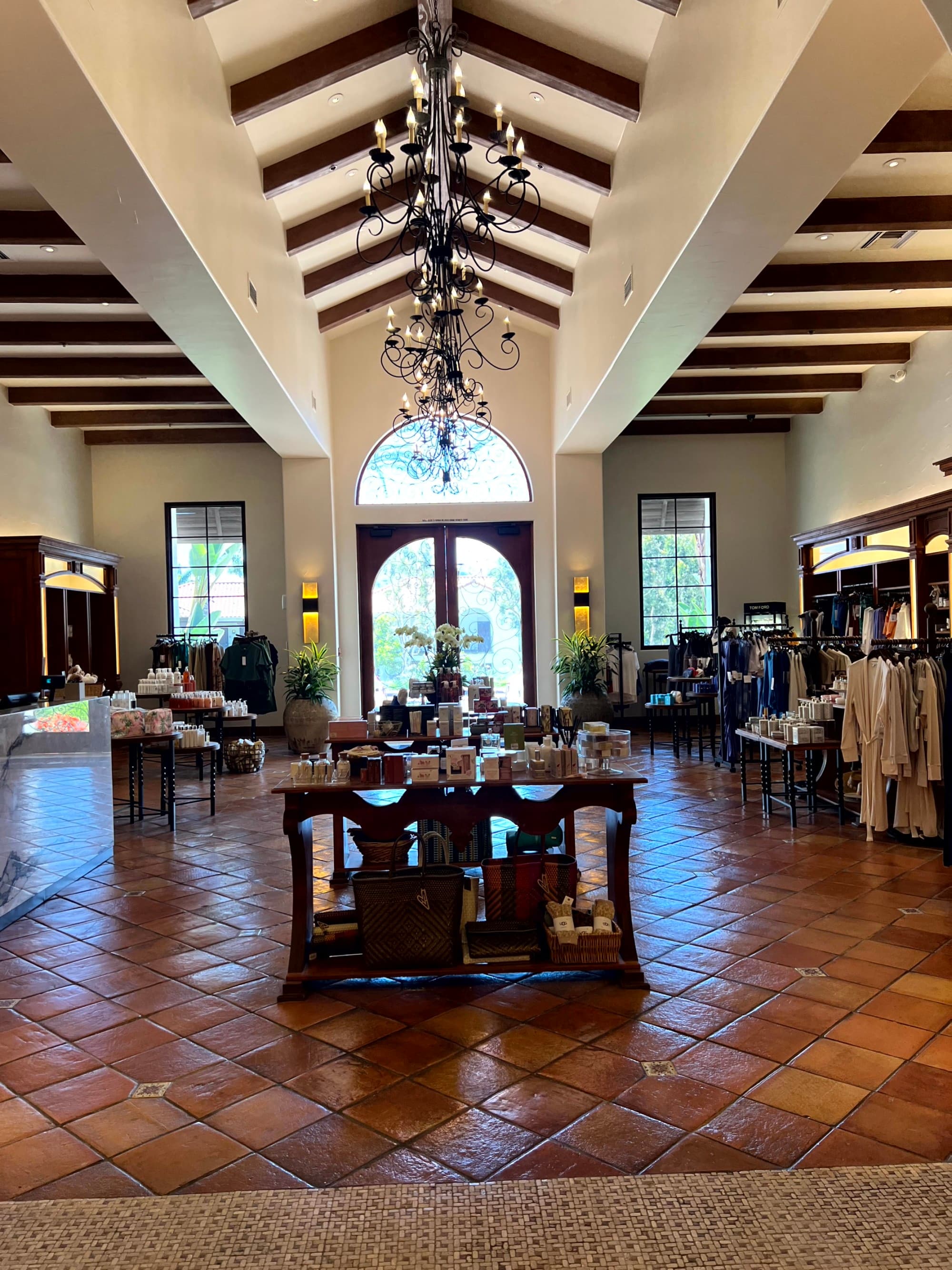 A gift shop with tables and racks of candles and robes, with chandeliers overhead.