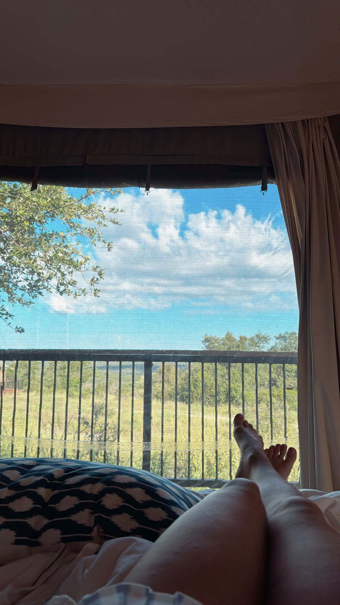 A persons legs cross on a bed overlooking a balcony outside a tent