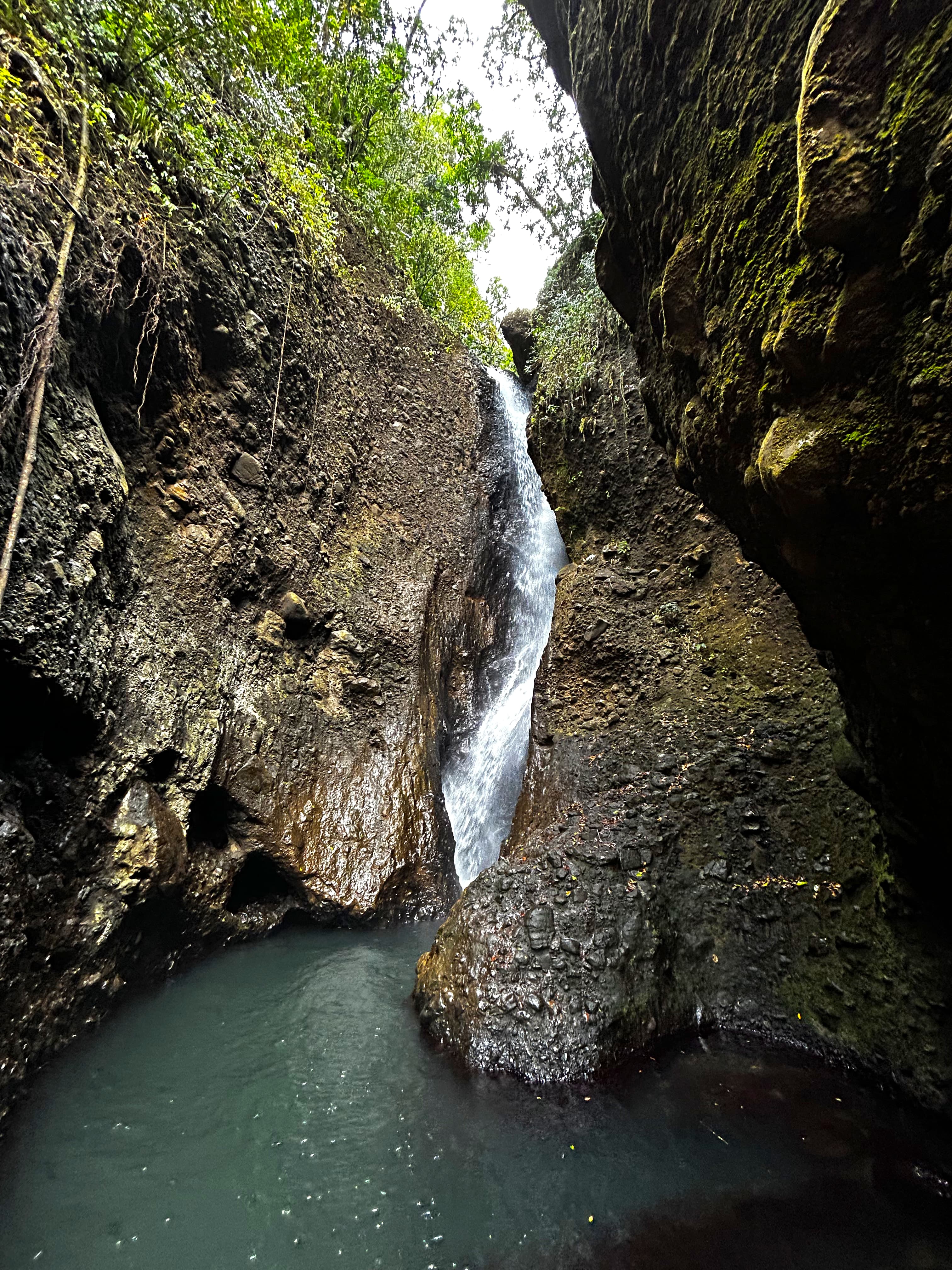 An image of a waterfall over a clear blue pool and rock formations.