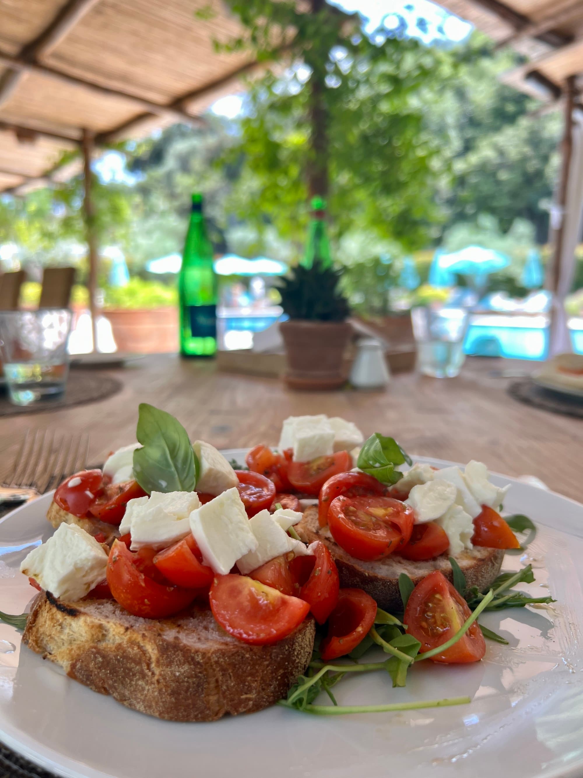 Tomato and cheese atop pieces of toast on a white plate, sitting on a table in an outdoor dining area