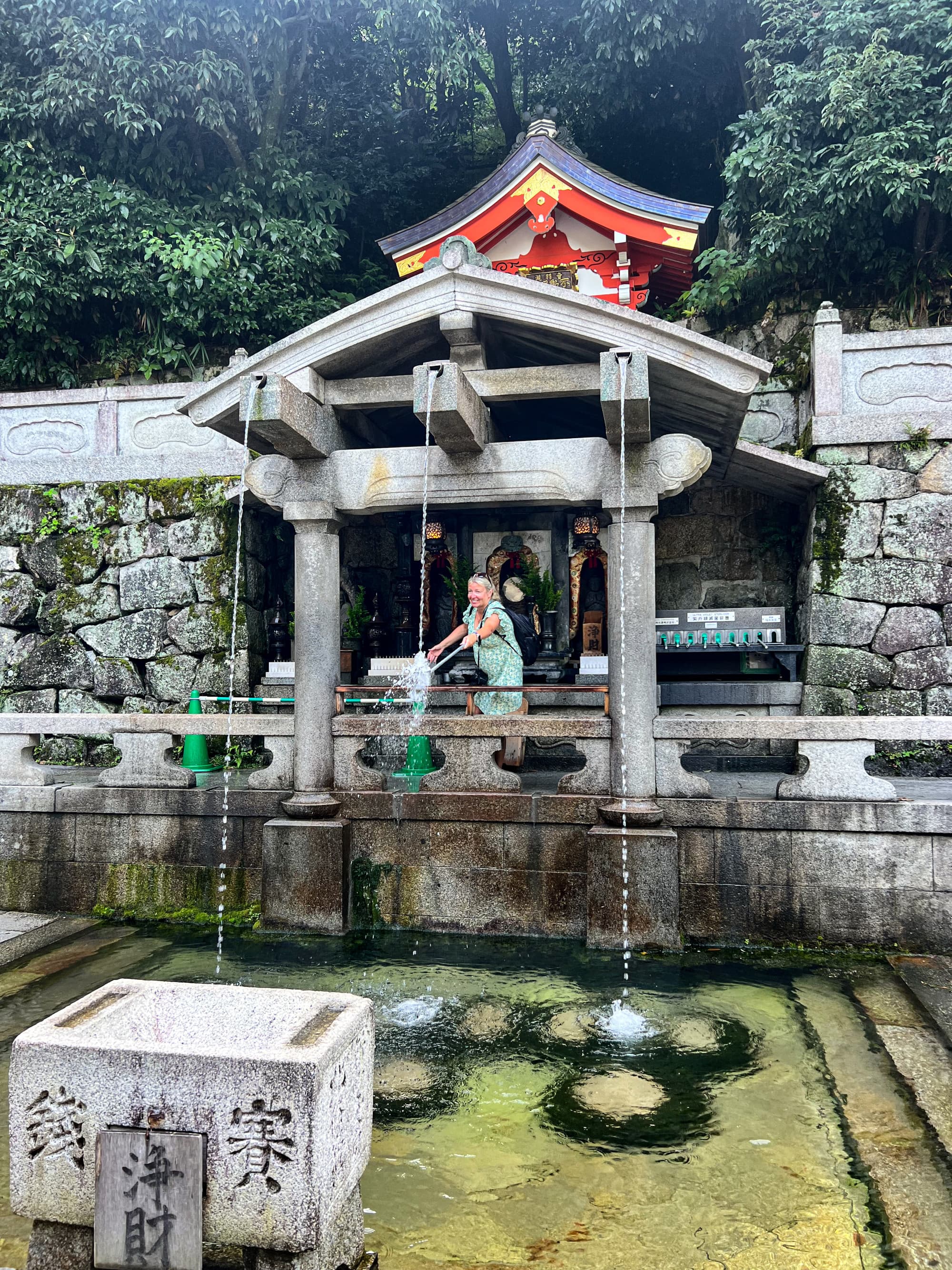 A Japanese shrine with a woman walking past a large fountain.