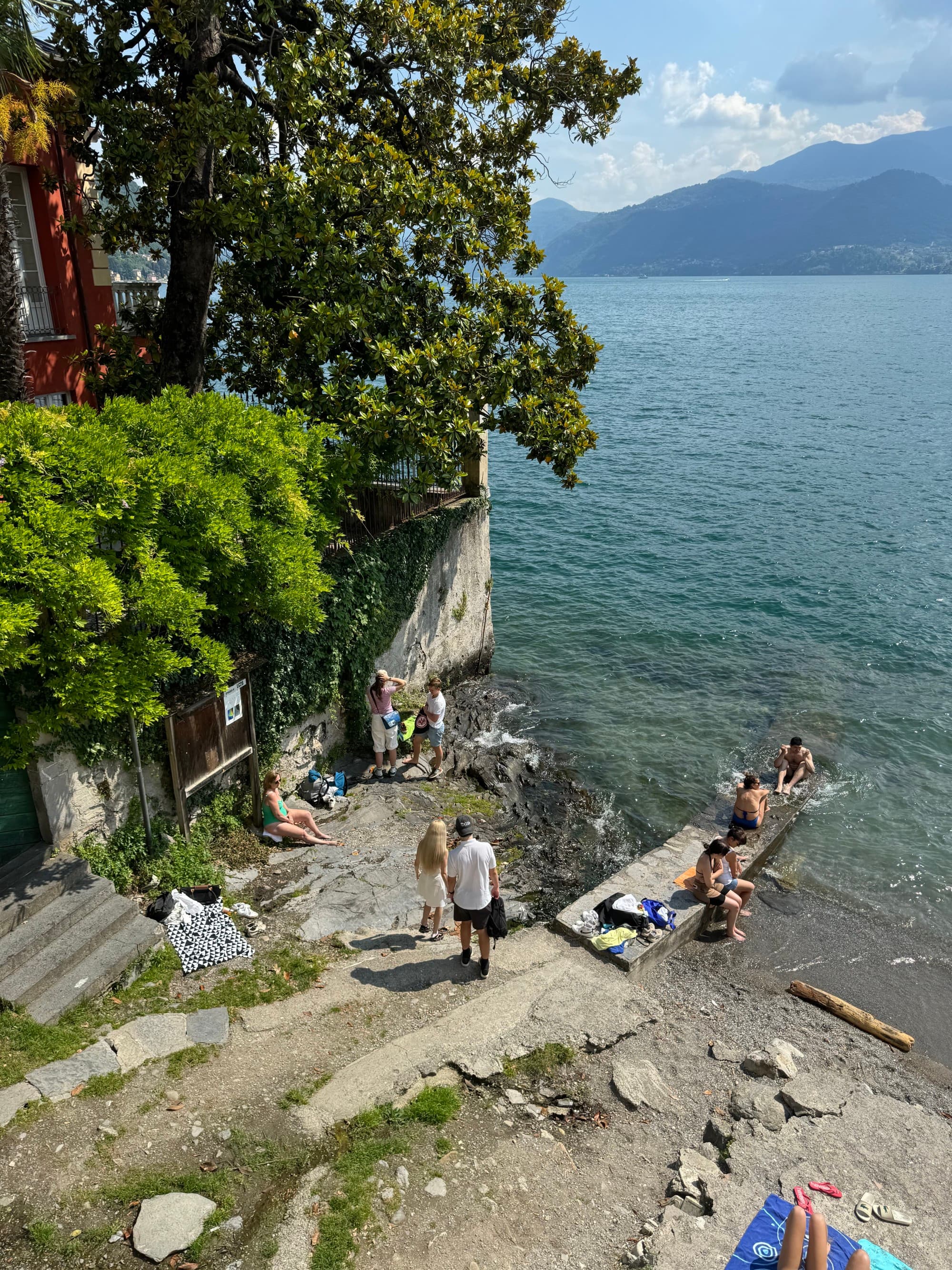 People enjoying the lake, a lush green forest on one side and mountains in the distance during the day.