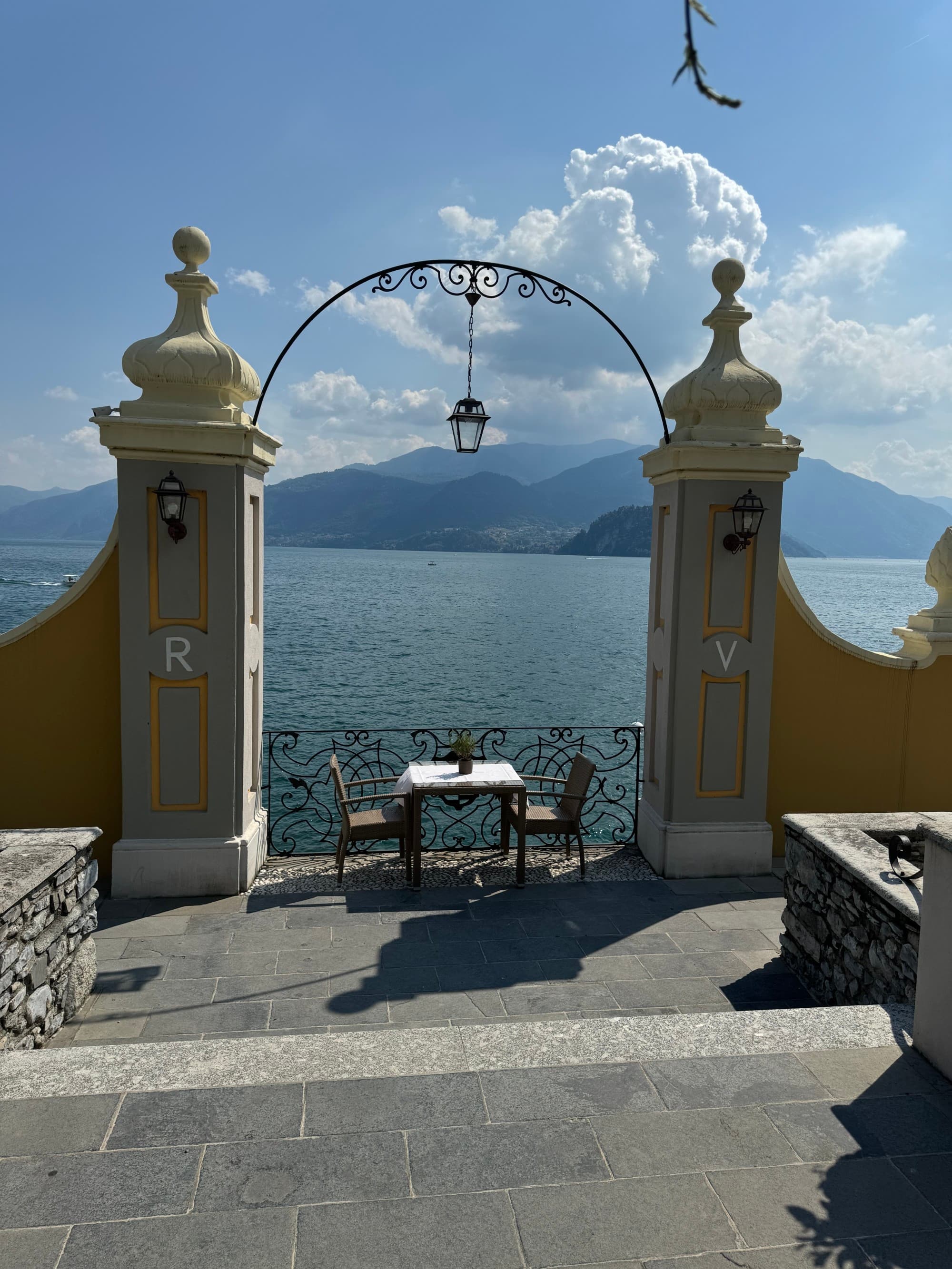 A view of the lake with a dining table and chairs under an archway with a lantern and stone pillars on either side in the foreground.