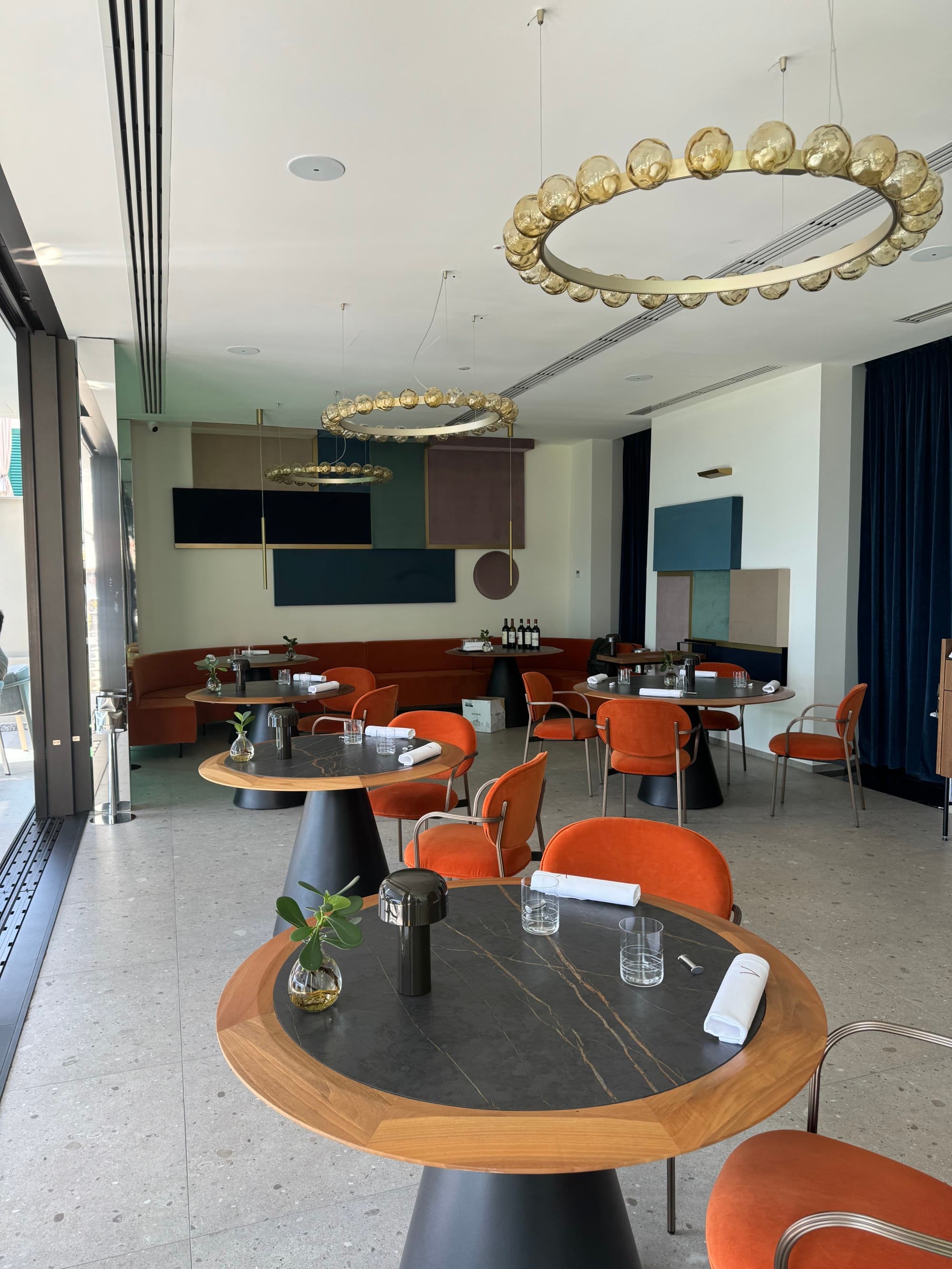 A view of a dining area with white floors, circular black and wood tables, orange chairs and red booths at Hotel Royal Victoria.