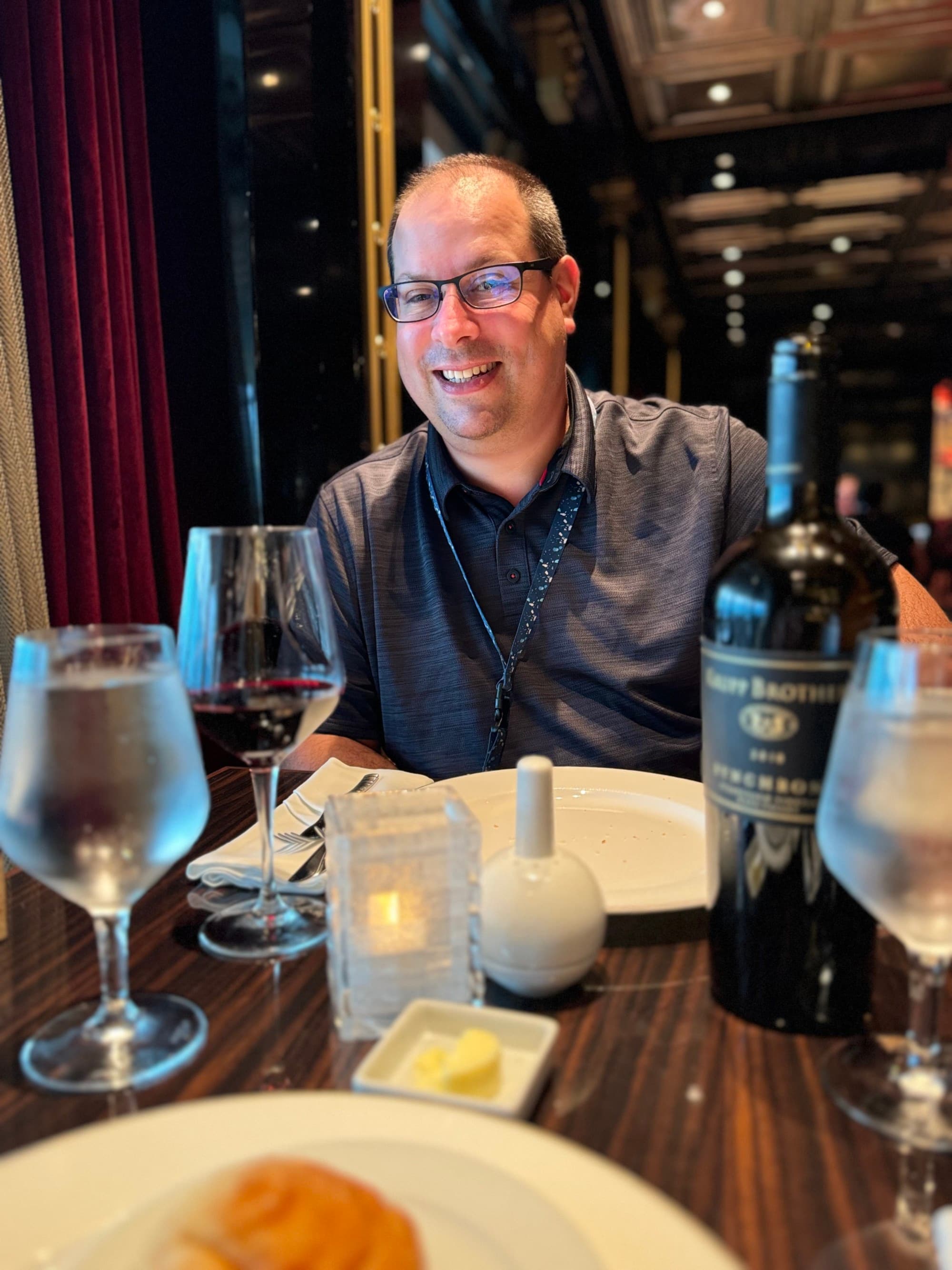 A man smiling and sitting at a dinner table with wine glasses and a wine bottle in front of him at Fahrenheit 555 Steakhouse