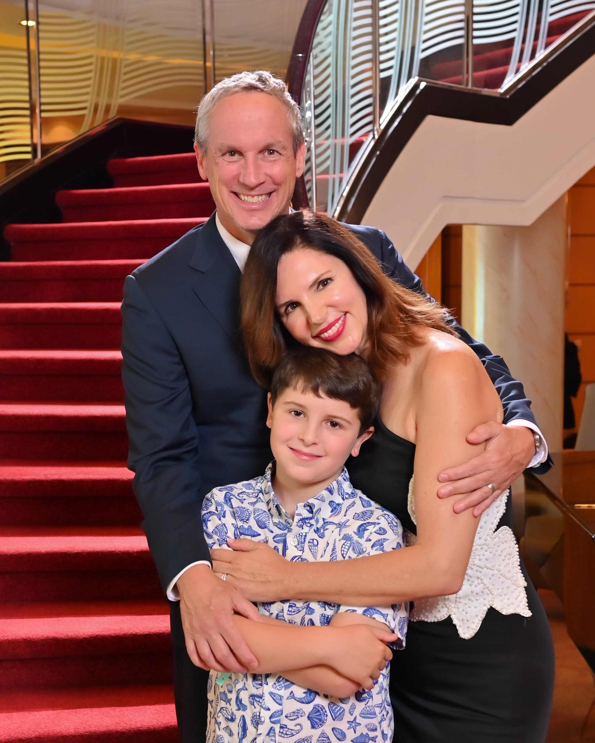 A family of three posing in front of red-carpeted stairs.