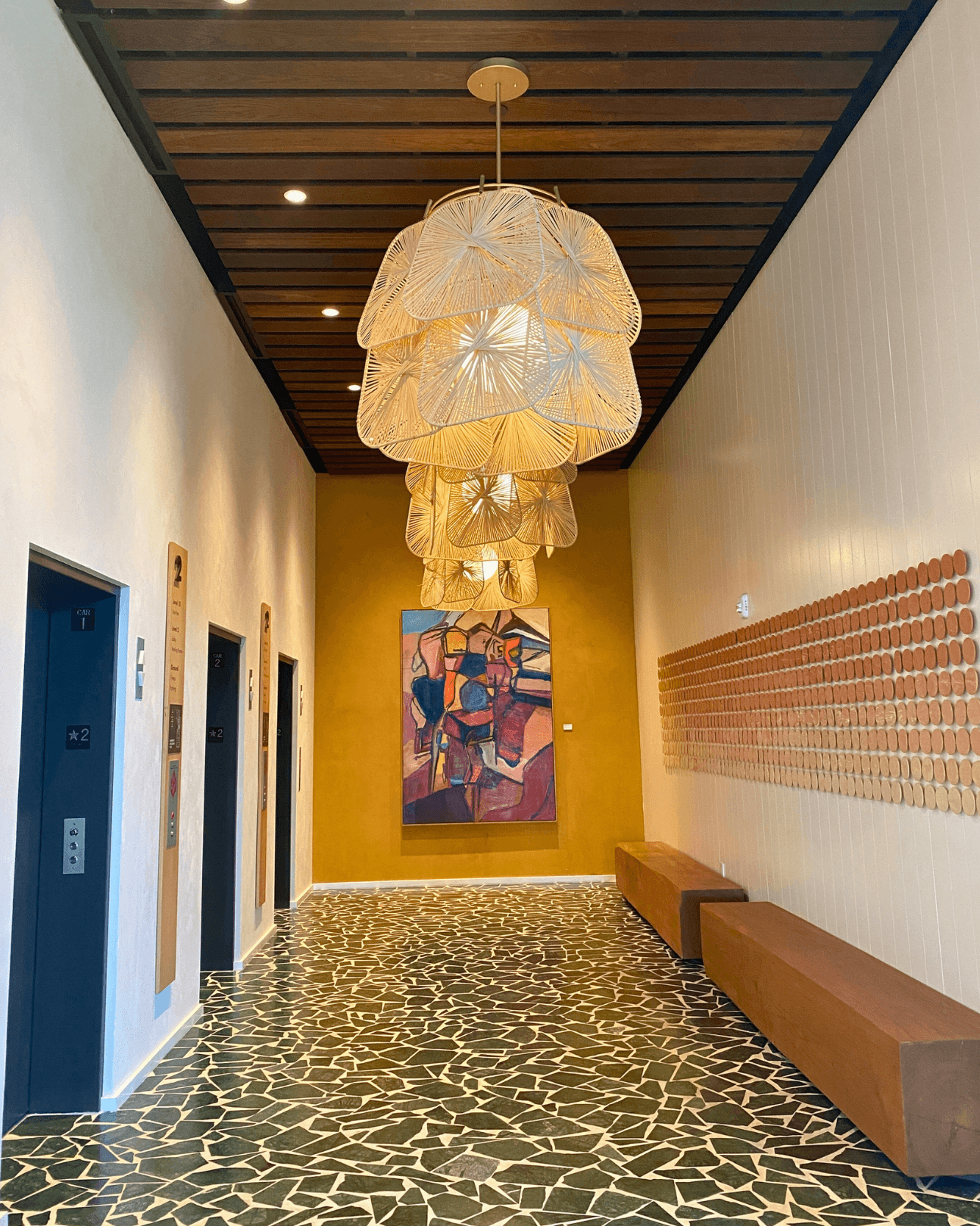 A lobby area in front of elevators with ornate light fixtures hanging from the ceiling and green patterned floors