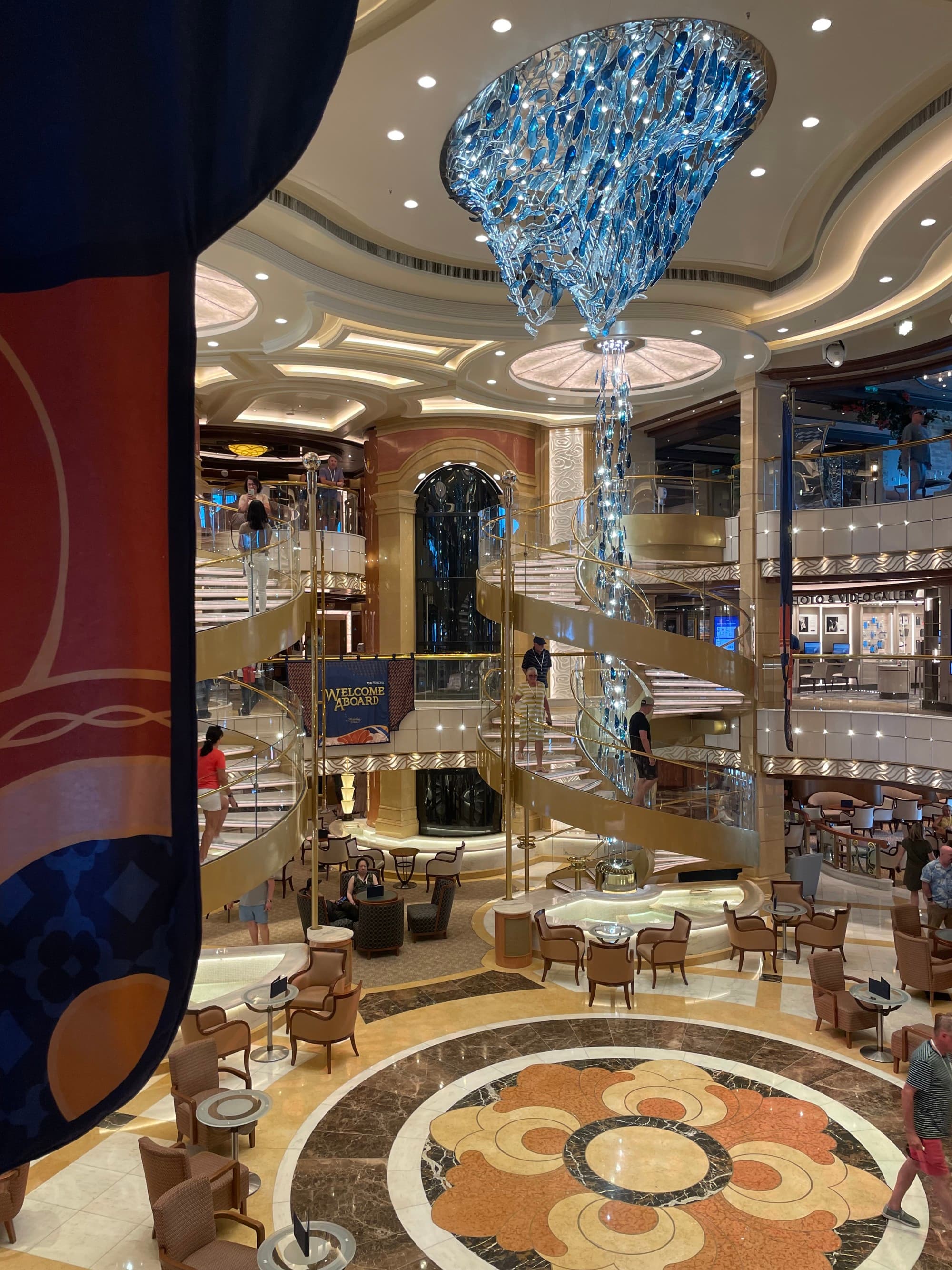 A lobby of a cruise ship with tall ceilings and an ornate light fixture