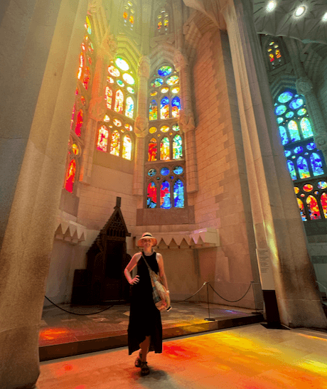 A person standing and posing for a photograph in front of a tall, stained-glass window inside a cathedral