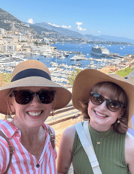 Two women smiling for a selfie photo with a seaside village in the background