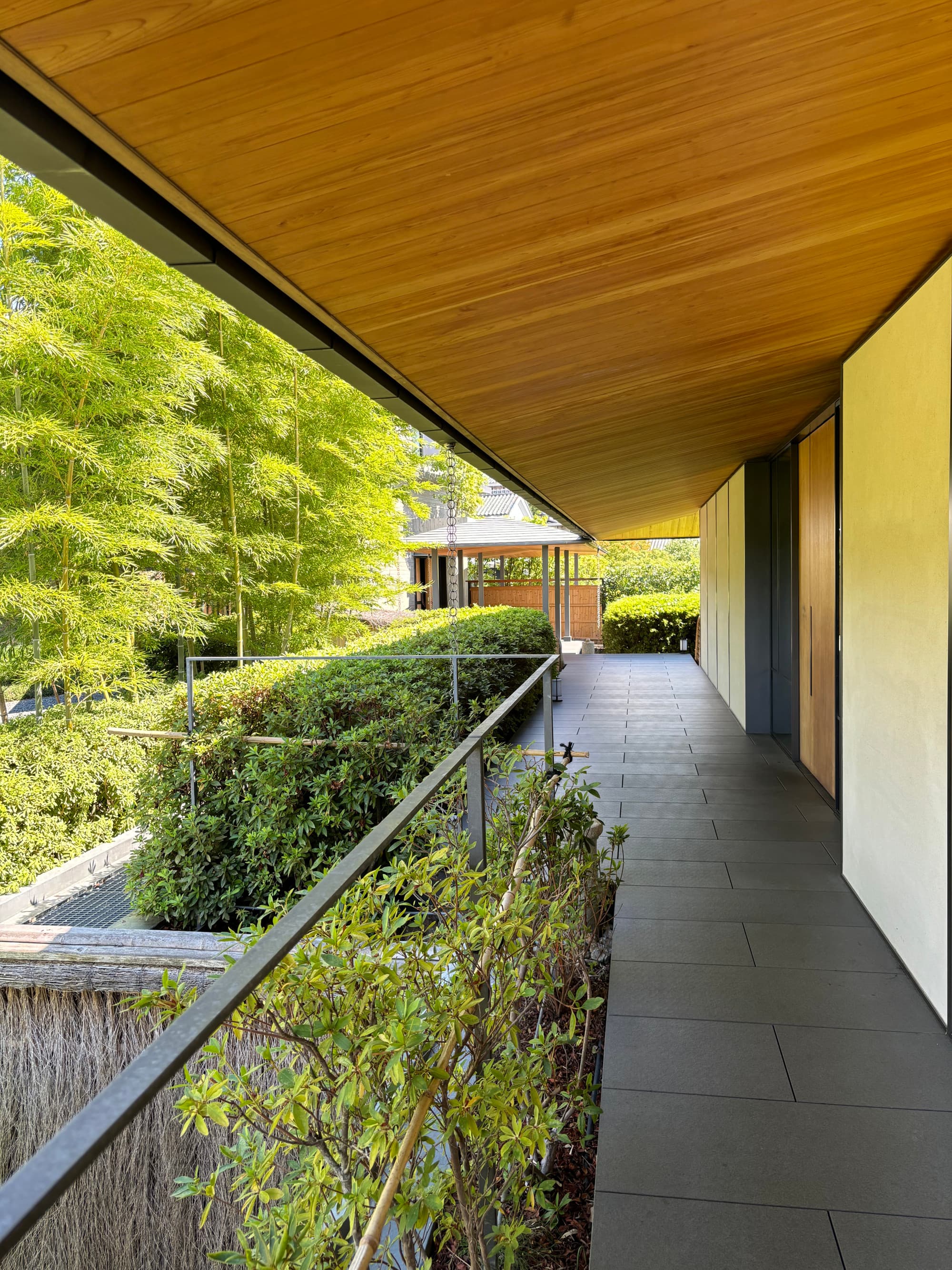 An outdoor hallway with green hedges against the railing