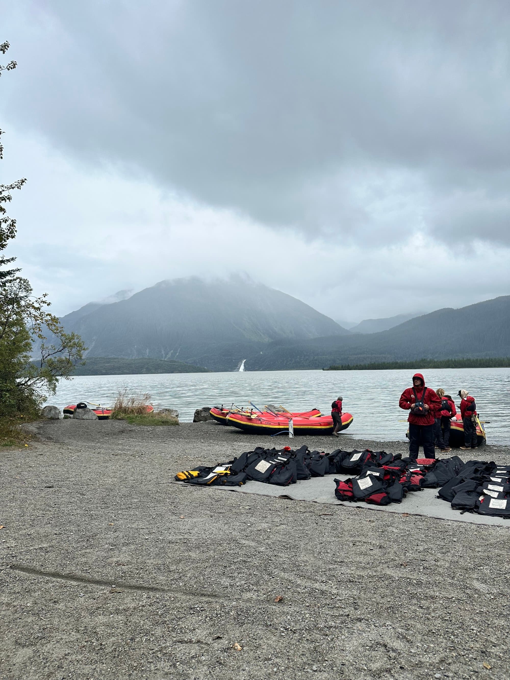 Wet suits laid out on the ground in front of a river with mountains in the distance