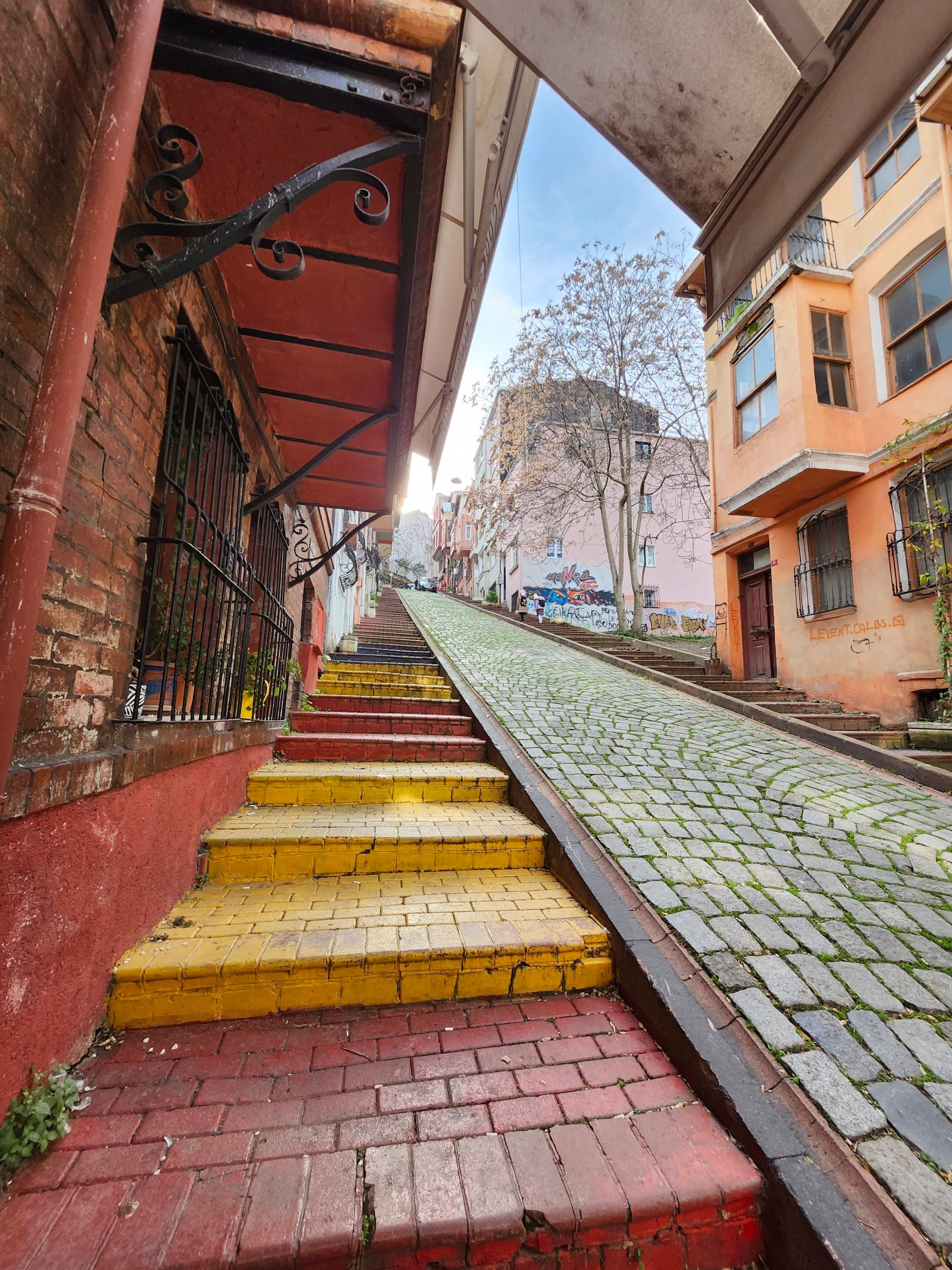 A set of red and yellow steps going up a hill alongside a steep road