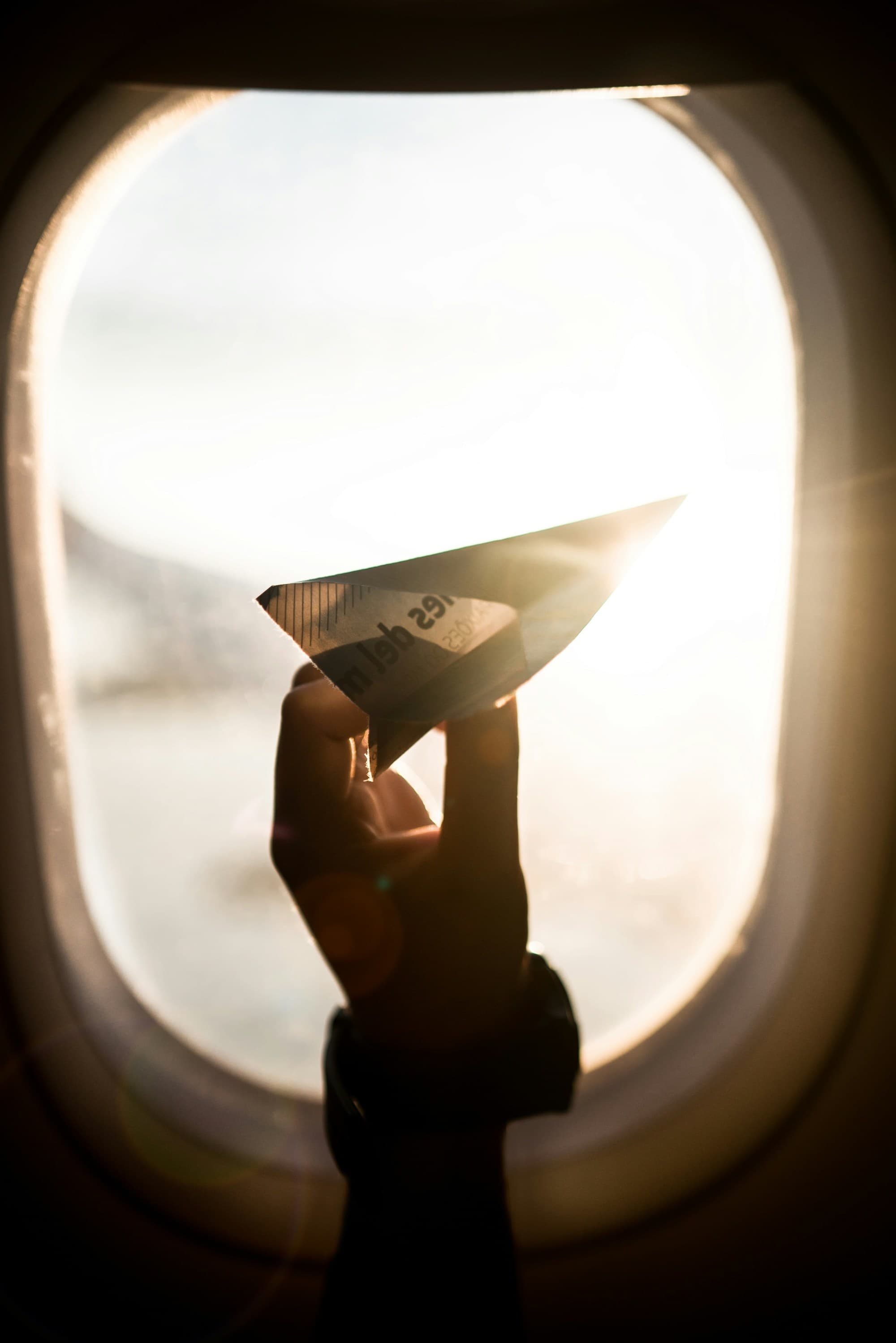 A child's hand holding a paper airplane in front of an airplane window