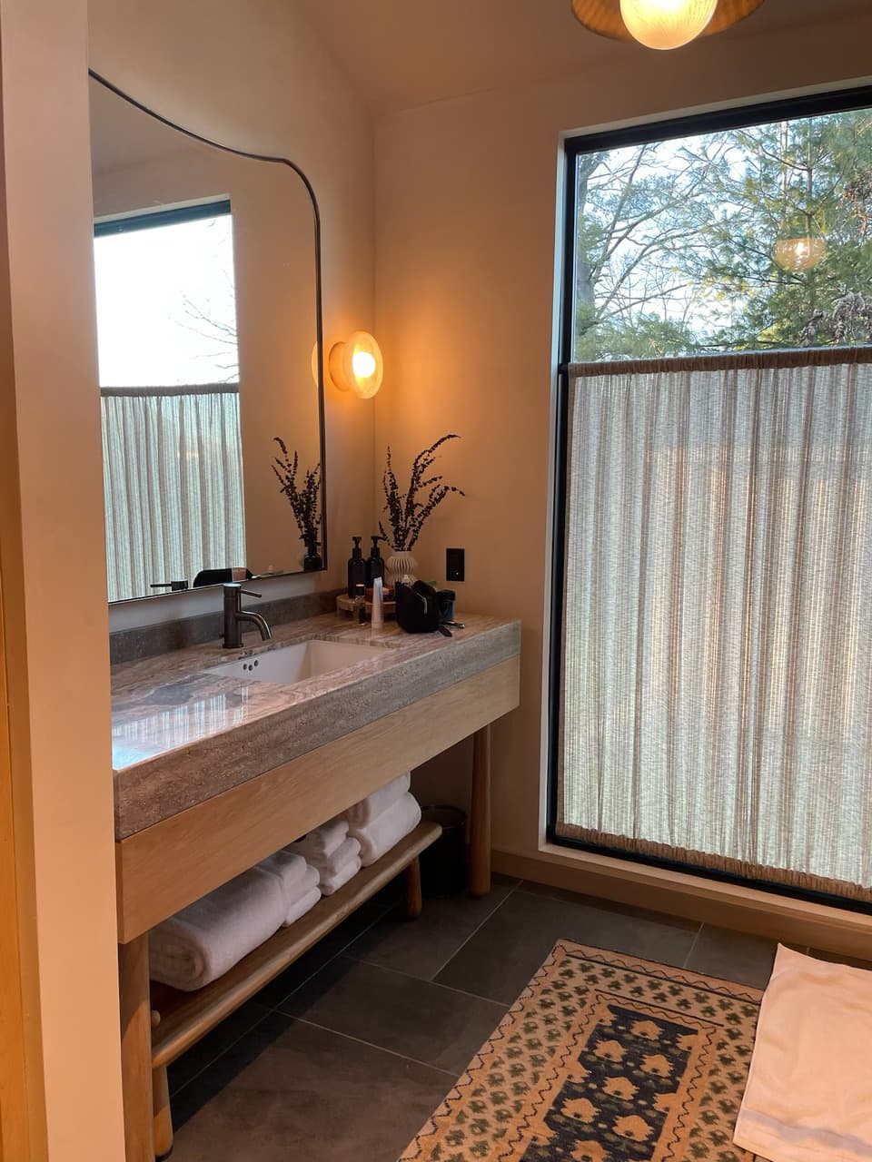 BOWER CABIN BATH a serene setting with a sink, marble counter top, rug, mirror and soft lighting.