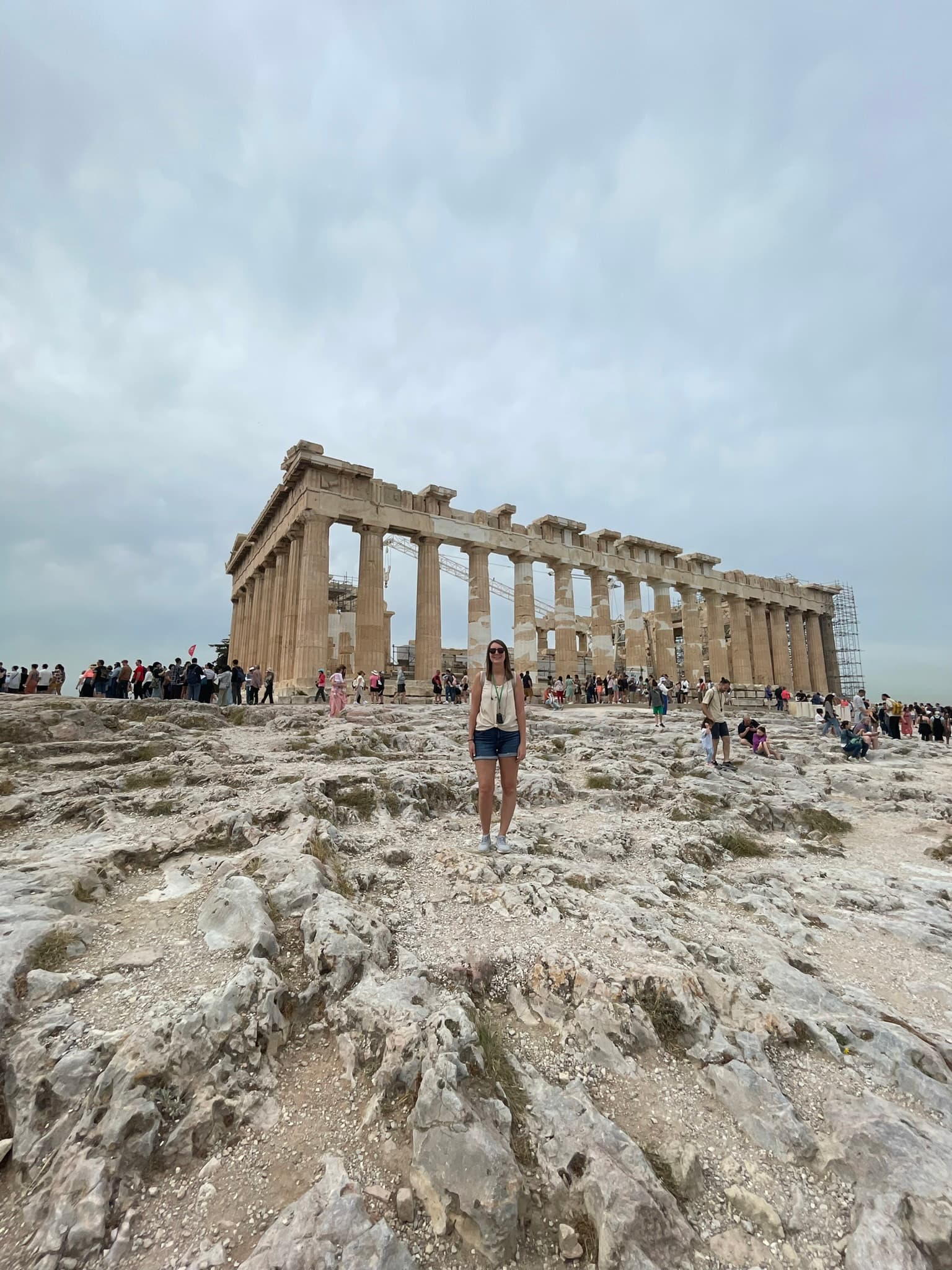 A woman standing in front of ancient ruins with cloudy skies overhead.