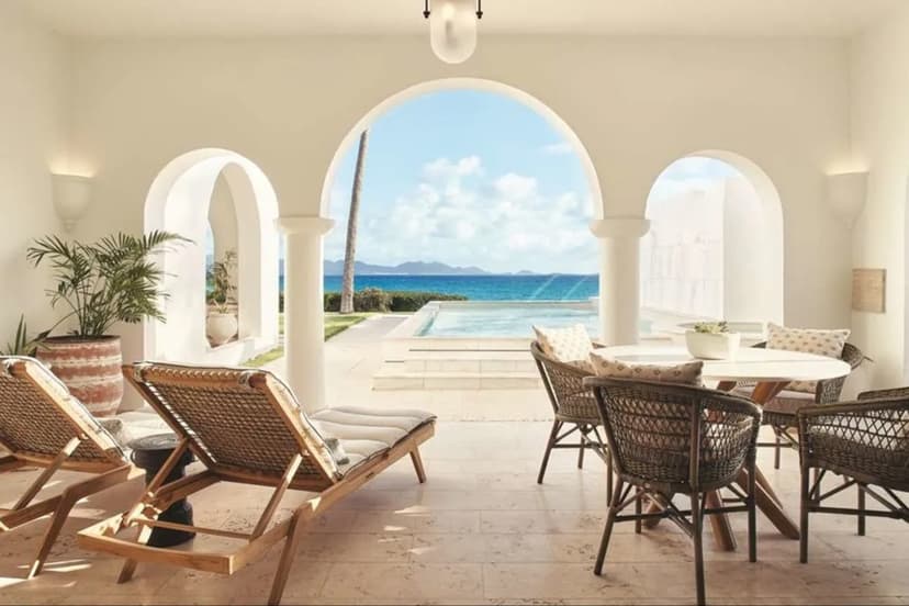 lounge chairs on a terrace looking through an archway to a pool with the sea beyond