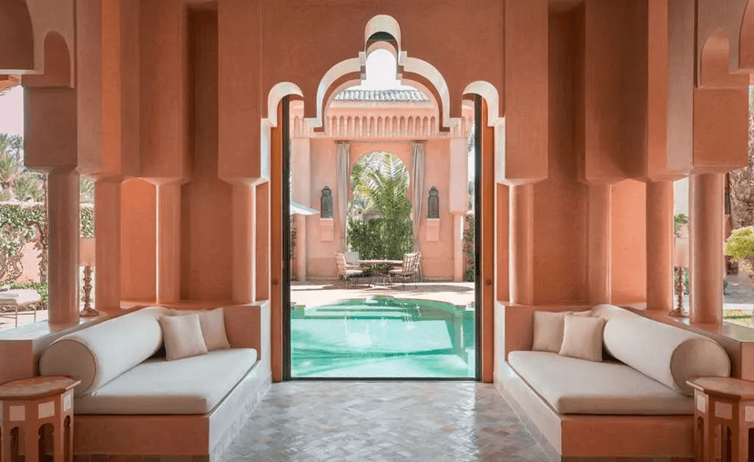 A courtyard at the Amanjena hotel, with pink walls, beige couches and a blue pool.