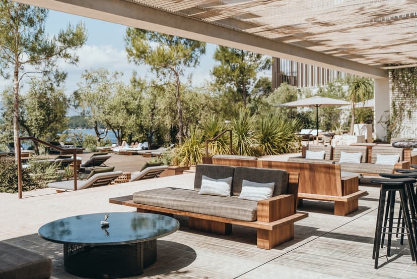 Lounge seating and tables on a sunny deck overlooking a pool at a resort.