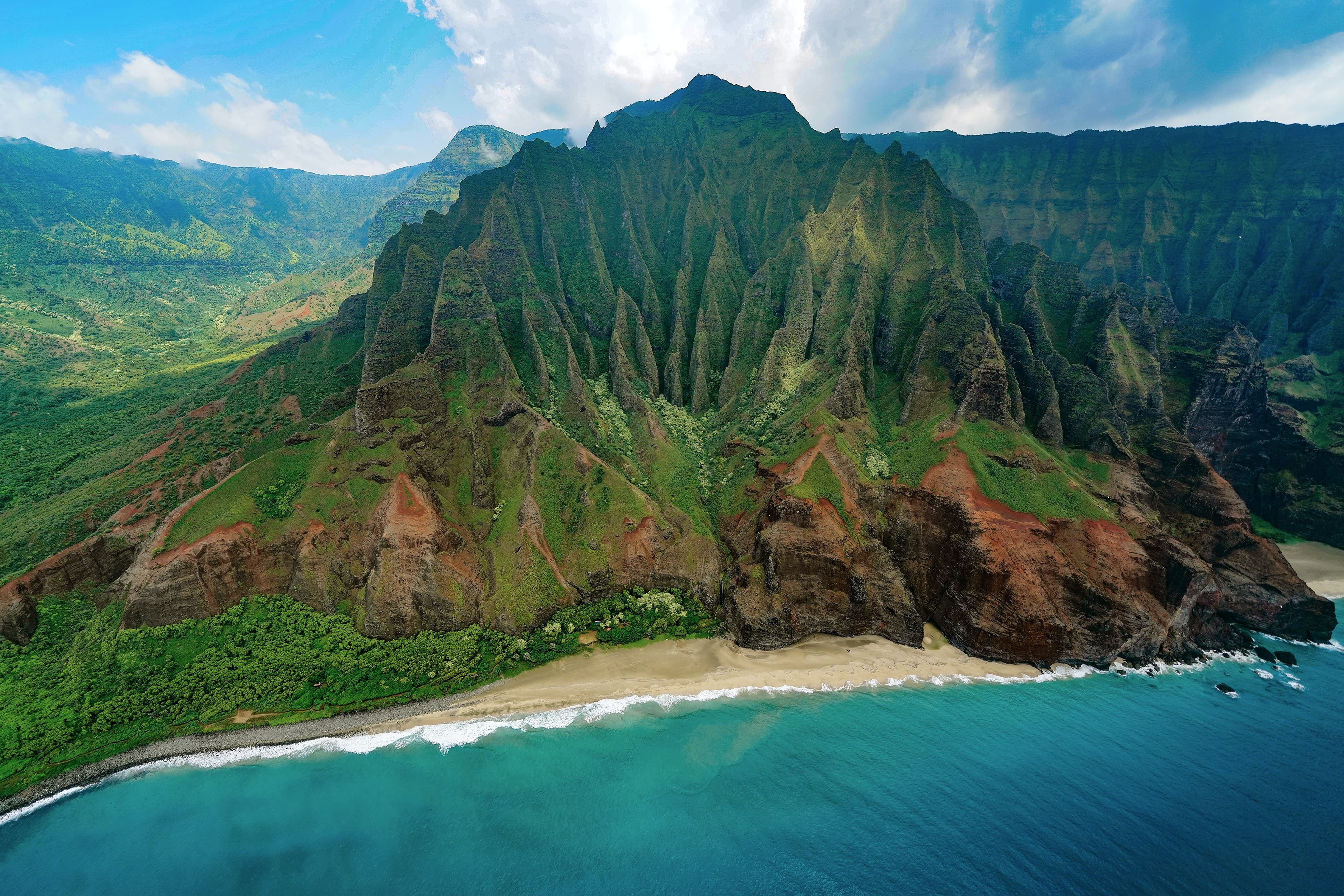 jagged green mountain next to beach and body of water