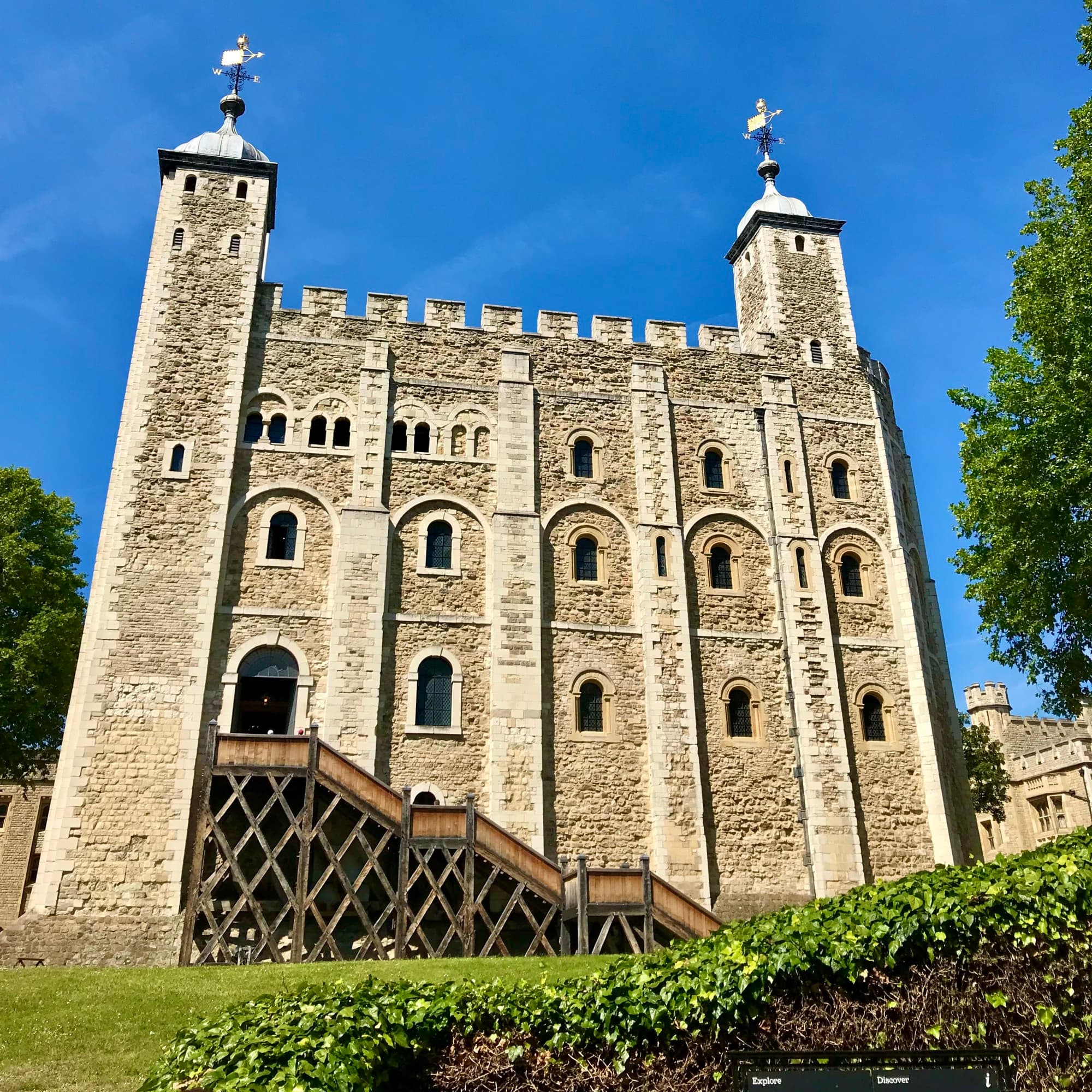 A stone tower in London with grass and tree next to it. The sky is a vibrant blue in the background.