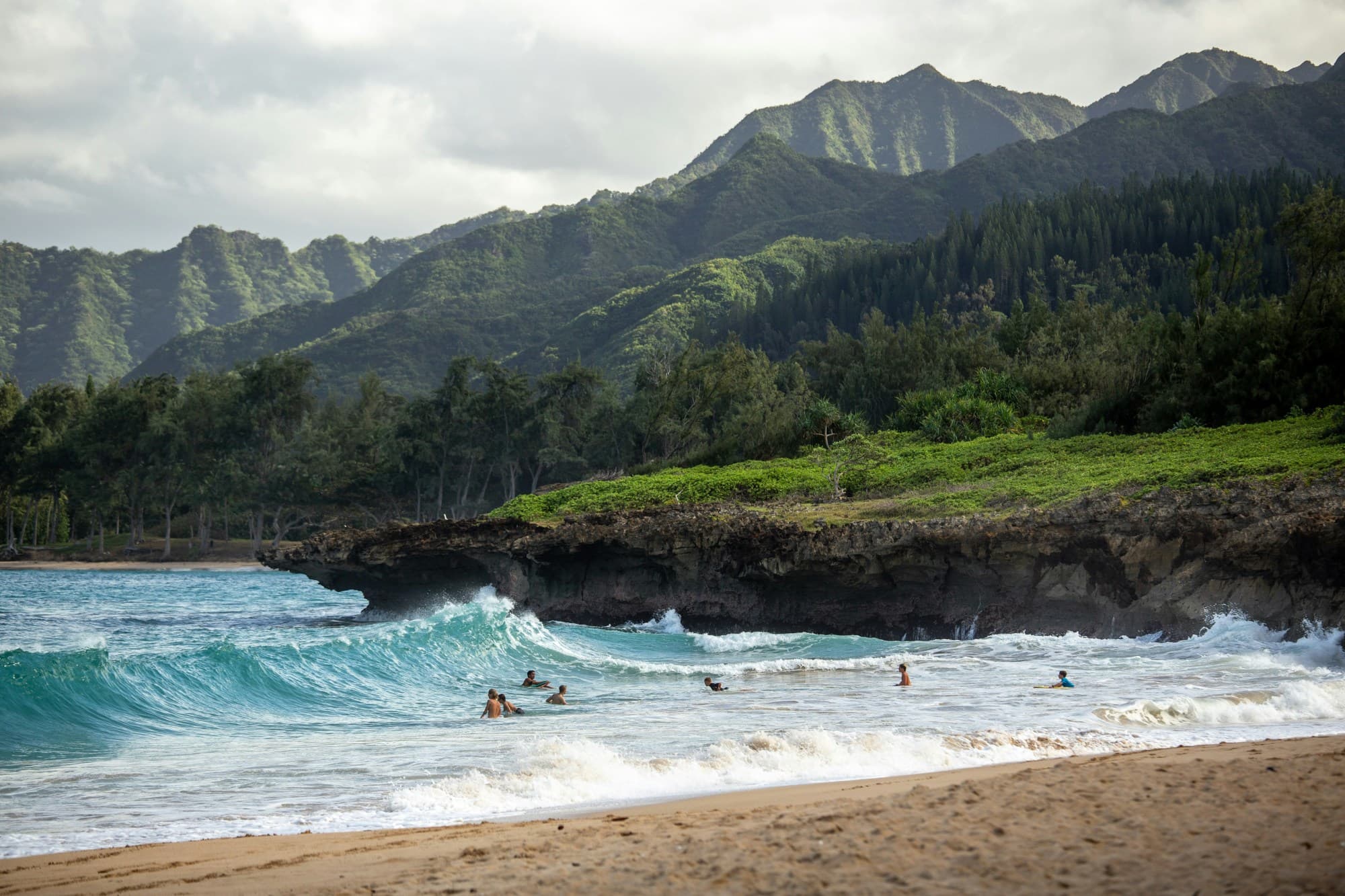 Surfers catching waves by a beach with green mountains in view