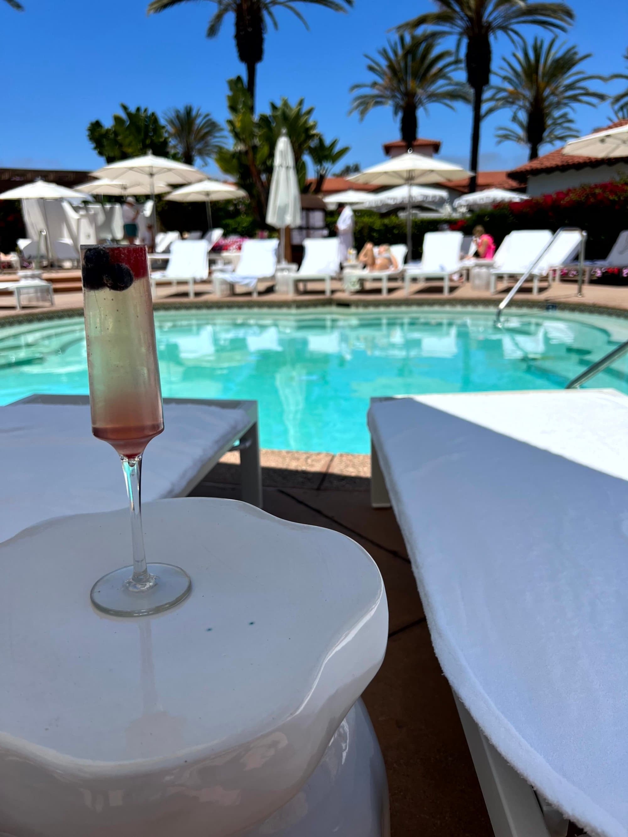 A fruity cocktail on a table by a pool lined with loungers at Omni La Costa Spa.