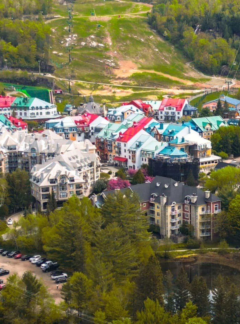 View overlooking a ski village in the summertime with green slopes and red and green buildings among the trees.