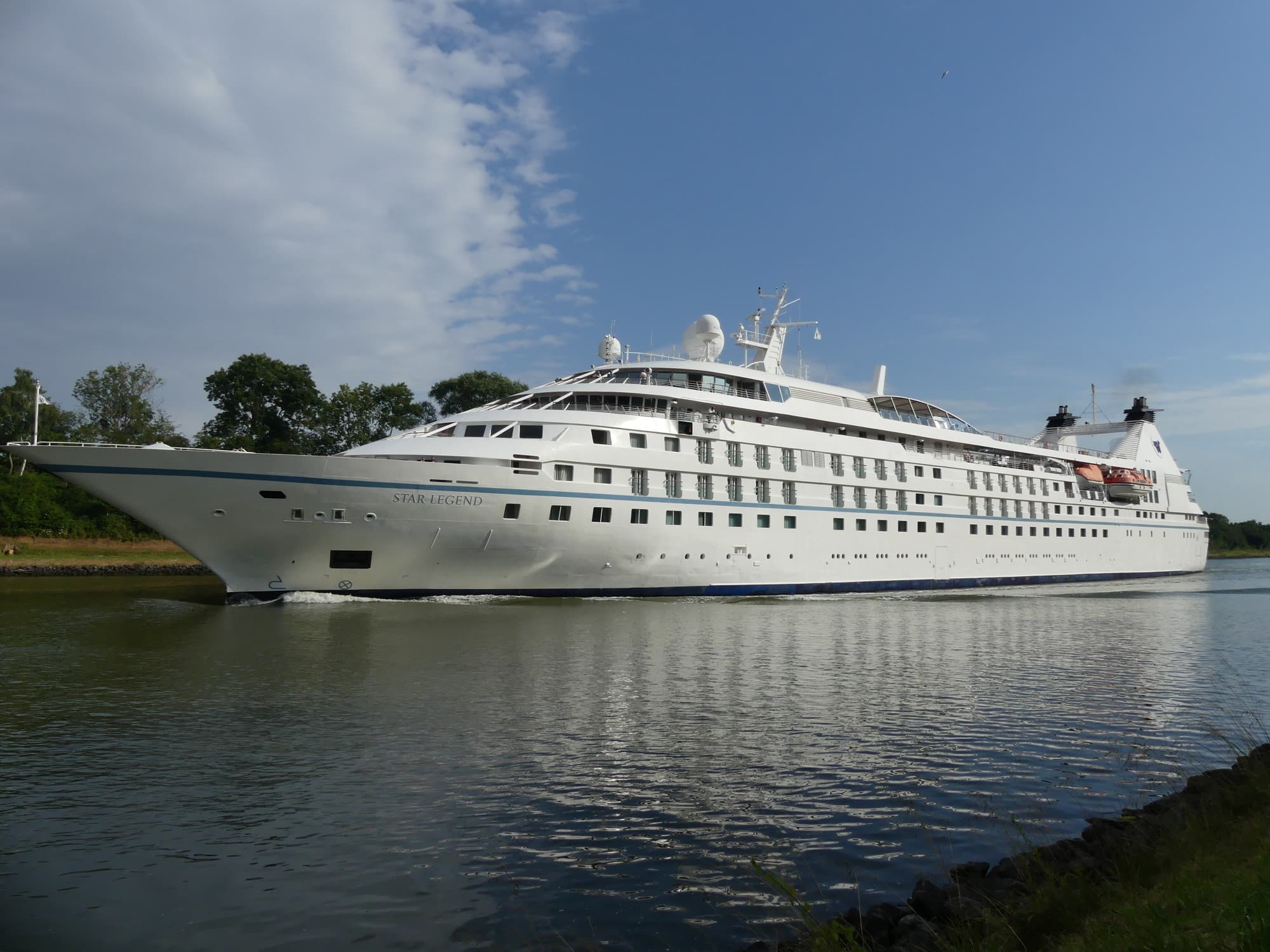 Windstar Cruises Star Legend Ship sits at port as the expansive vessel reflects in the water below on a sunny day.