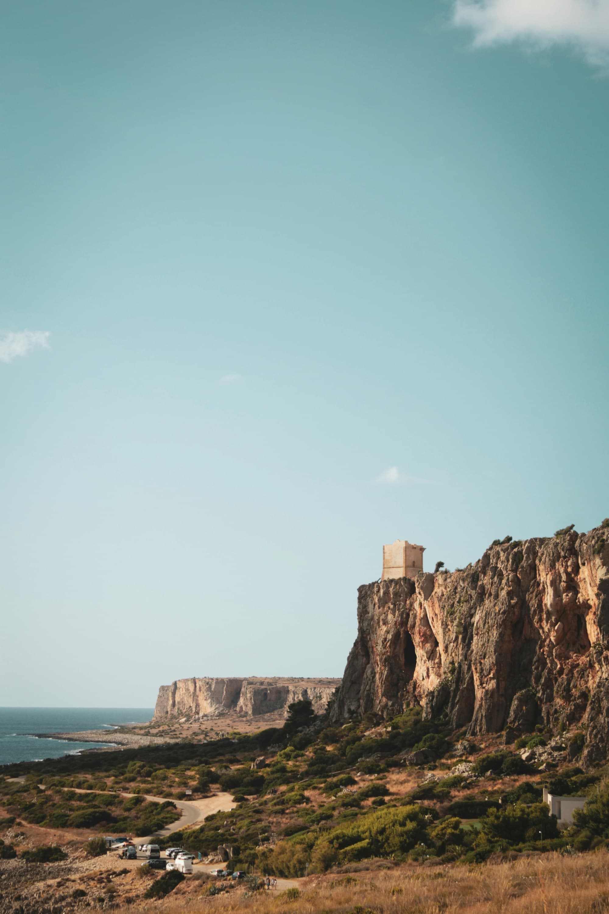 A view of striking cliffs and the ocean against a clear blue sky in Sicily.