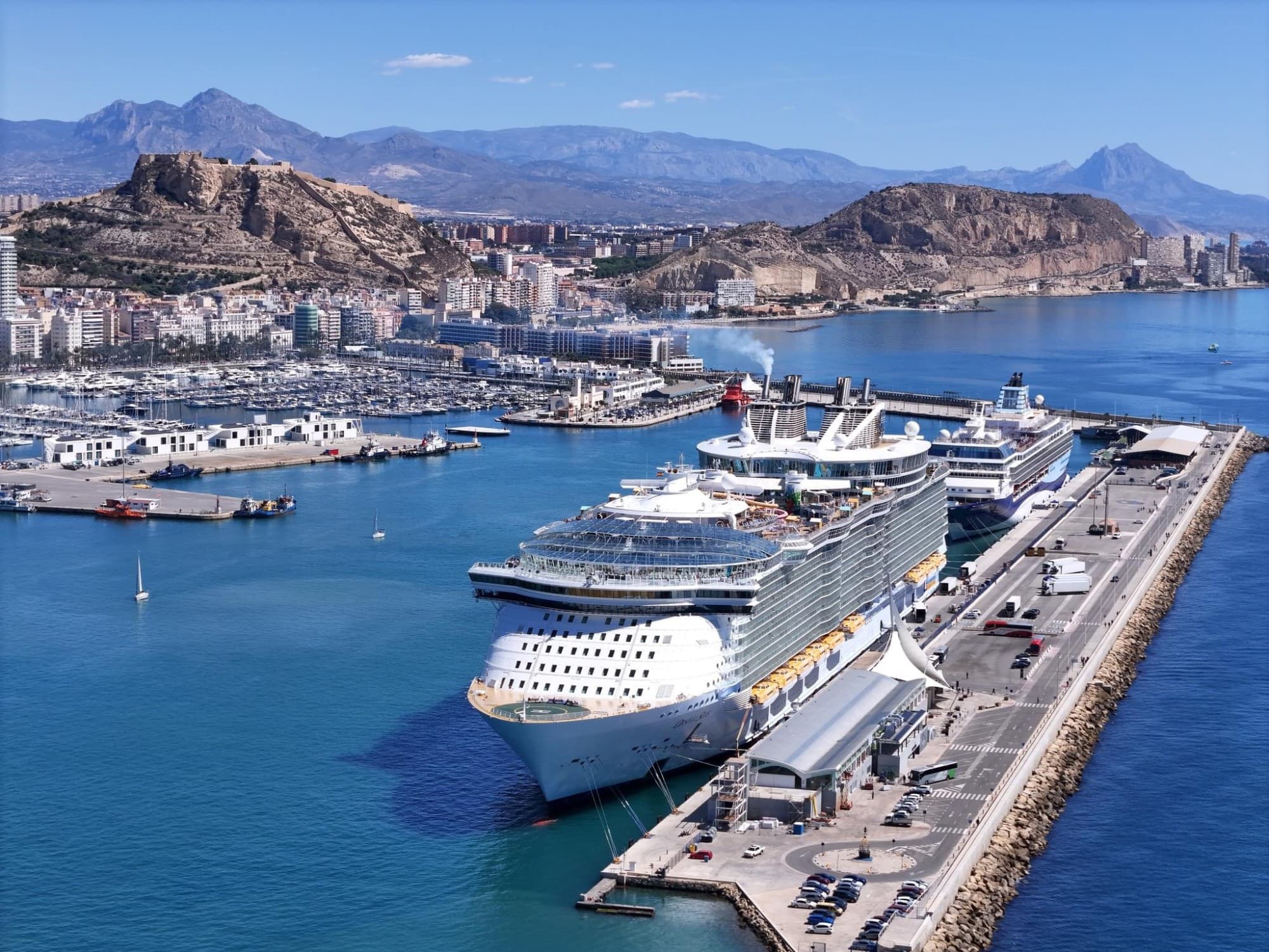 Aerial view of a cruise ship at a dock with mountains in the background.