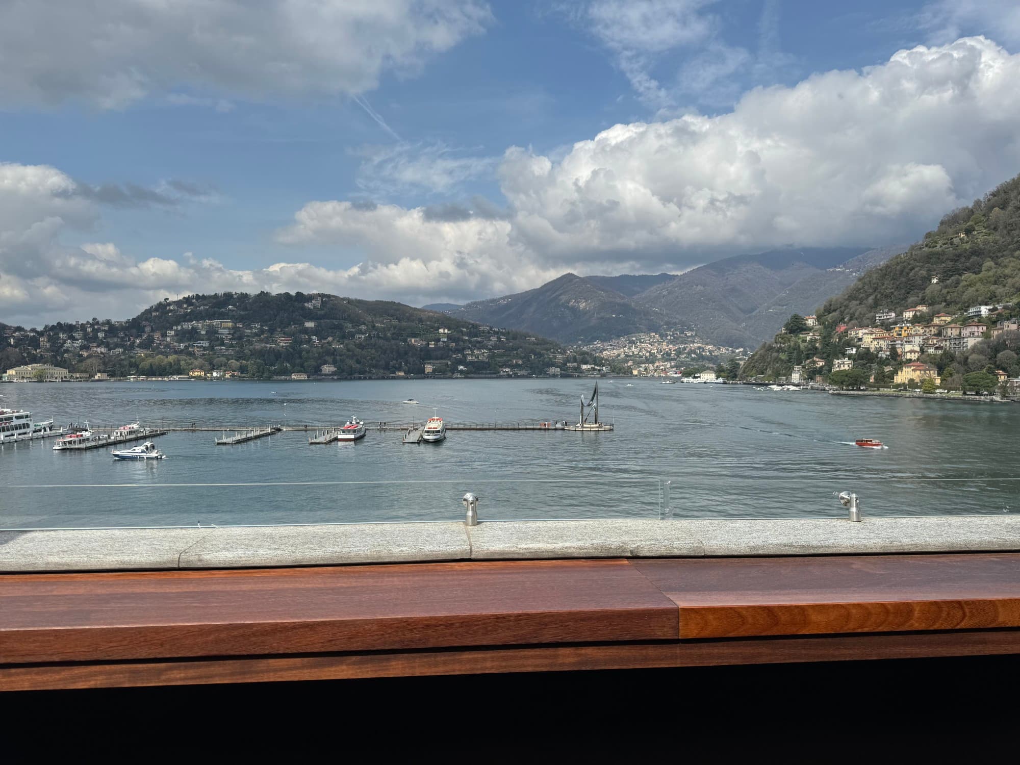 A photo of Lake Como with boats sailing across it and a mountain on each coast of the lake.